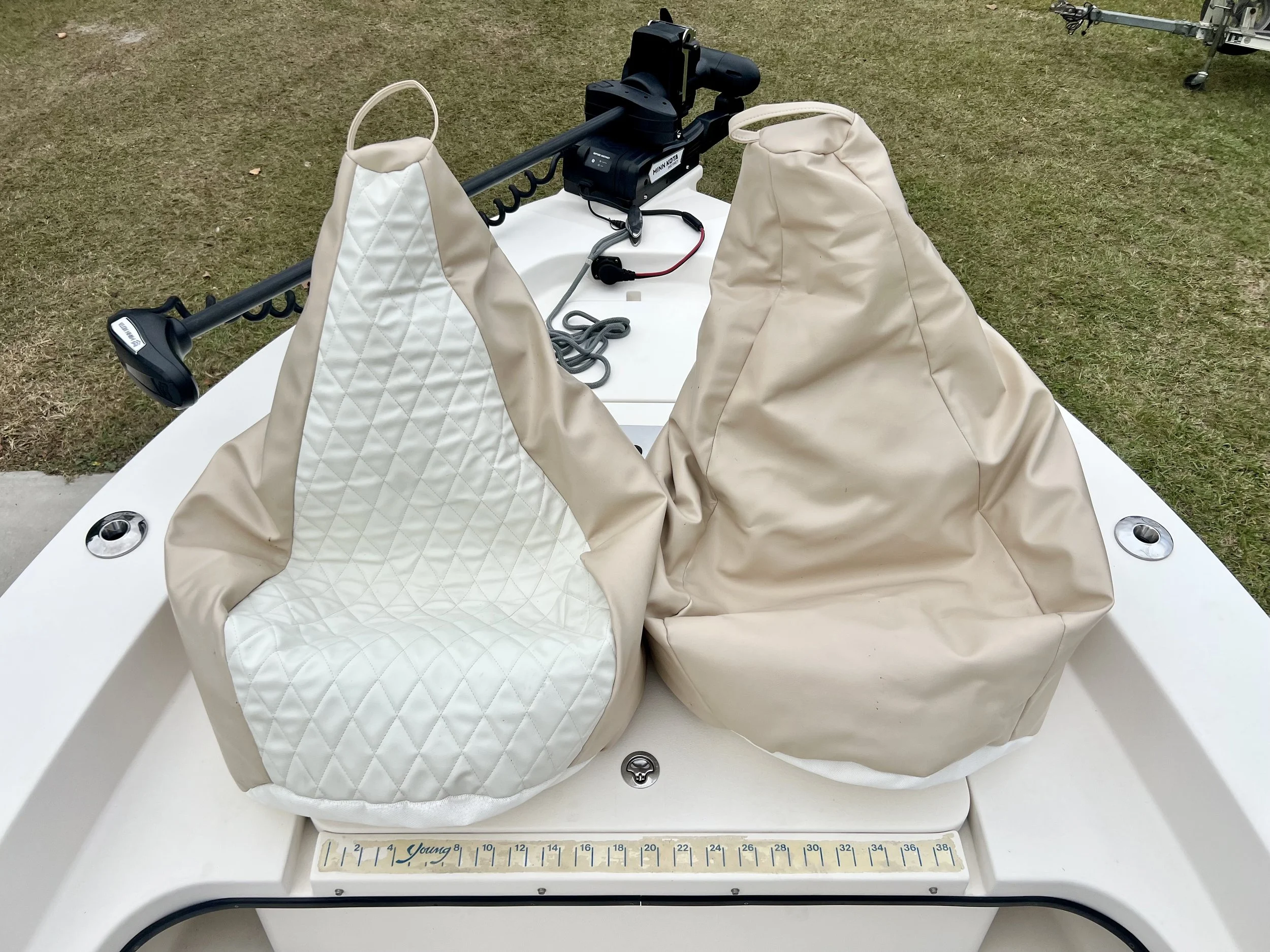 Two beige and white padded boat seats on a white boat deck with a measuring ruler and boat hardware, outdoors on grass.