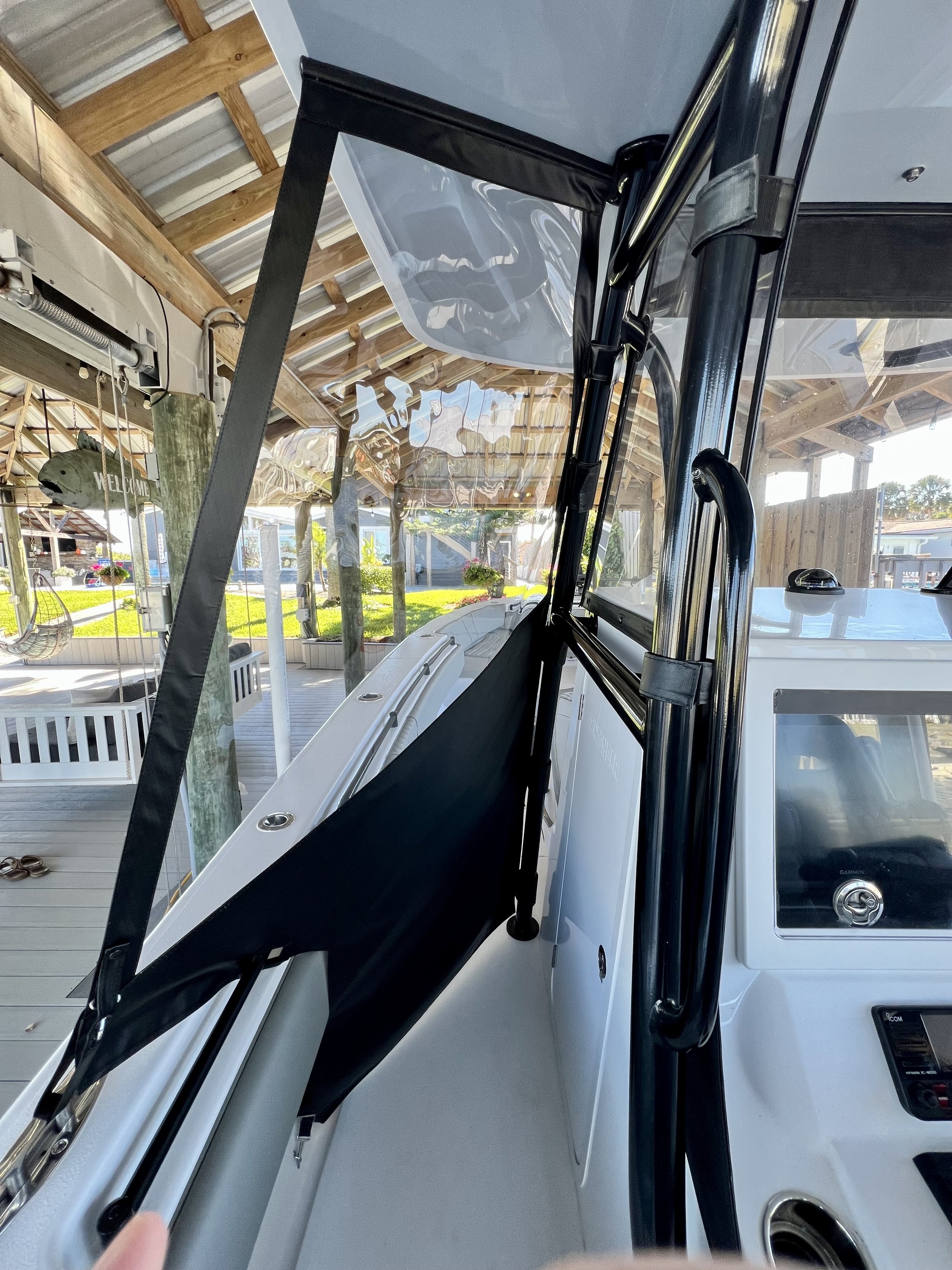 Close-up of the interior of a boat, showing the windshield, steering console, and a black canopy frame, with a view of the outdoors through the windows.