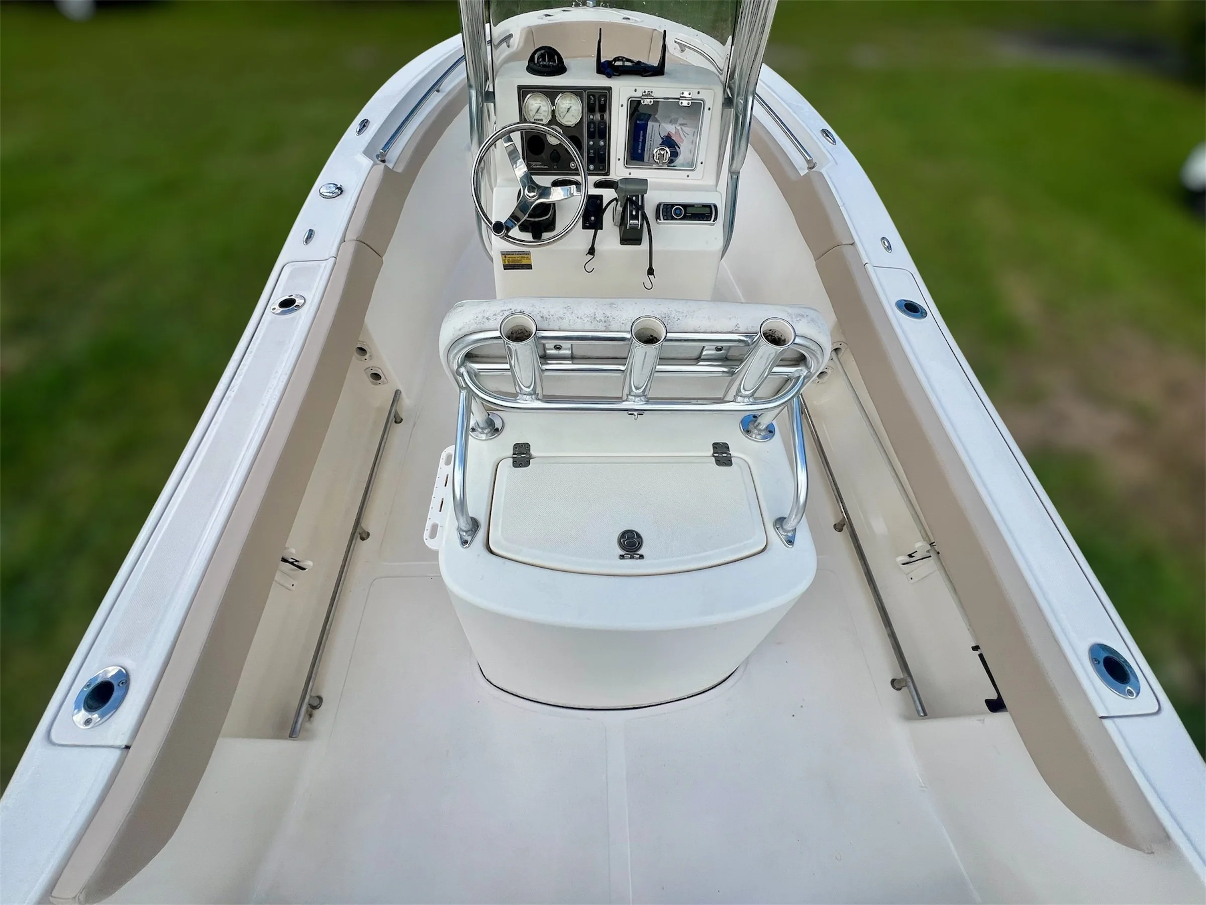 View of a boat's bow with steering console and rod holders, overlooking a grassy area.