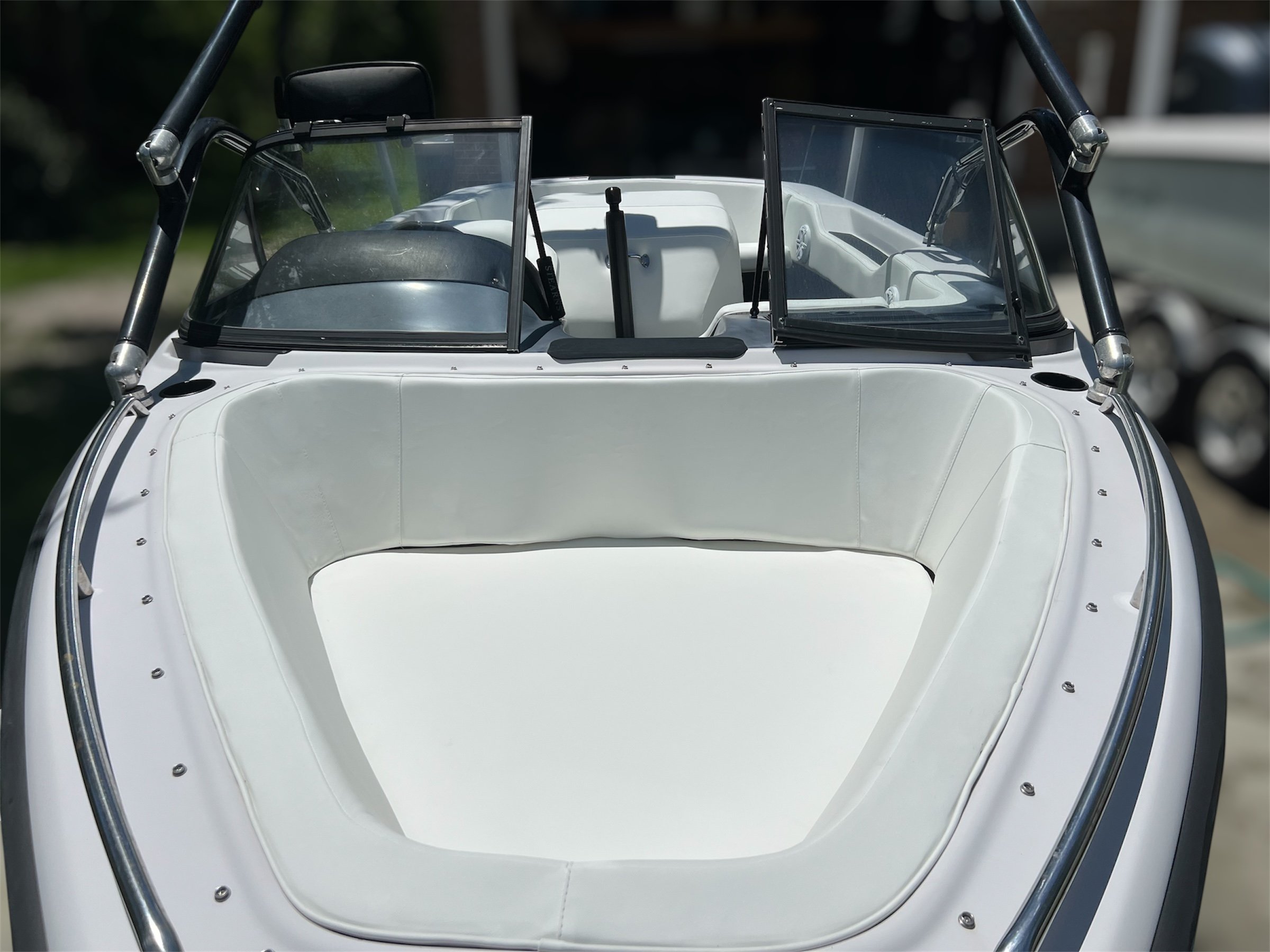 Front view of a white speedboat with a spacious cushioned seating area and a dashboard with steering wheel, and windshields on either side.