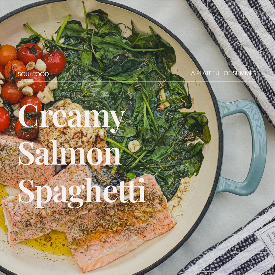 Raw salmon fillets seasoned and placed in a skillet with spinach, cherry tomatoes, and garlic.
