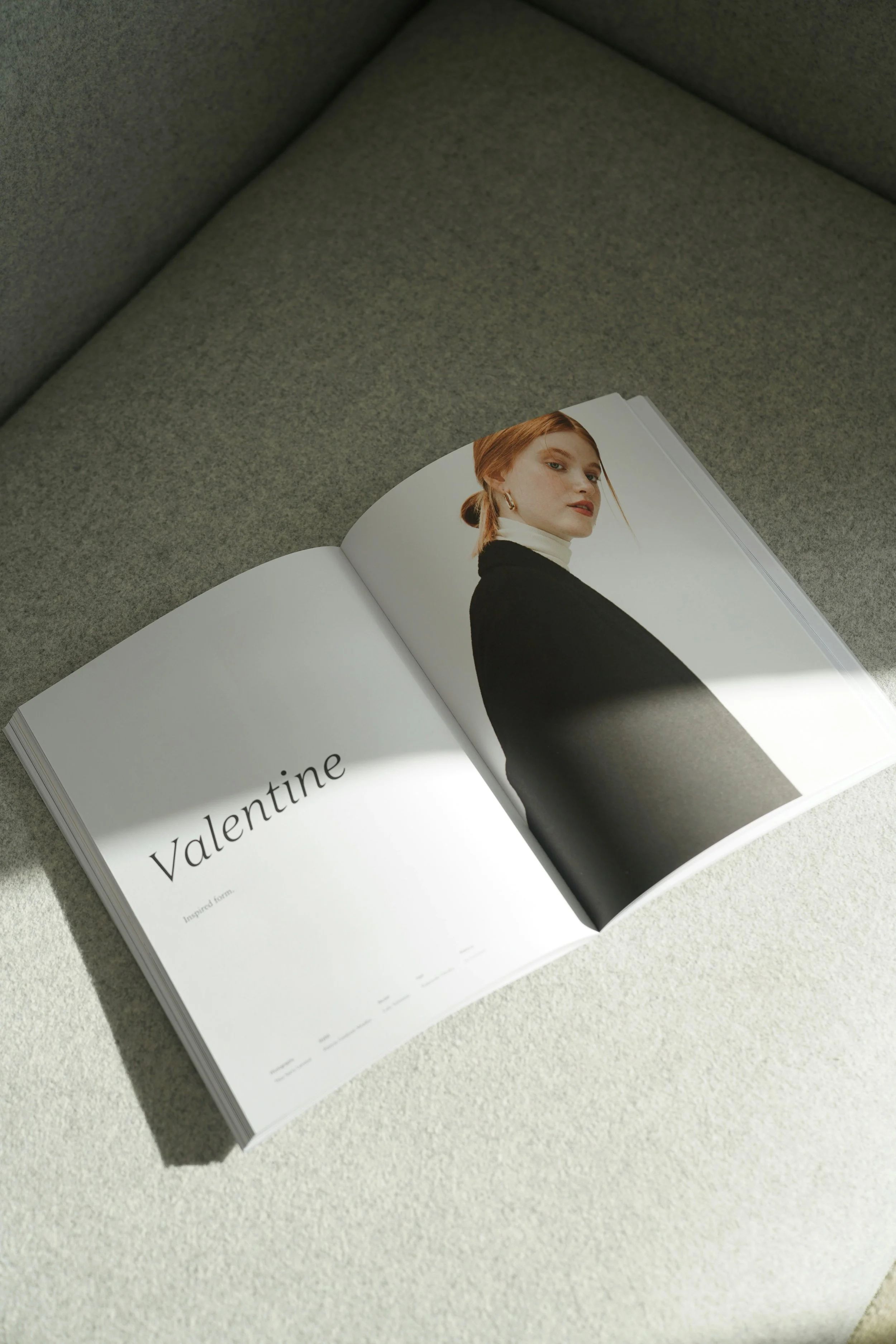 Open magazine on a light-colored surface, showing a two-page spread with a large portrait of a woman on the right page and the word "Valentine" and some text on the left page.