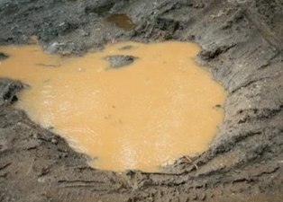 A small crater filled with muddy water surrounded by dirt and rocky terrain.
