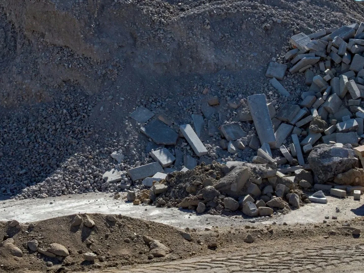 A construction site with a large pile of rocks, gravel, and broken concrete on a dirt ground, with an uneven surface.