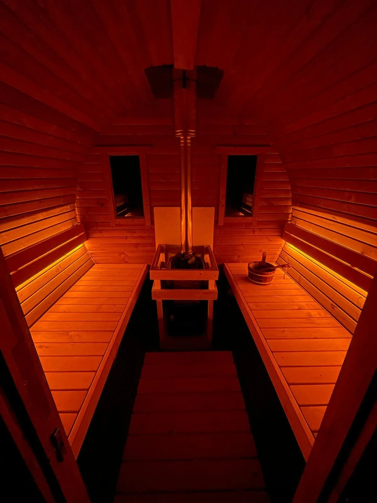 Interior of a traditional Finnish sauna with wooden benches, a sauna stove, and a bucket with a ladle.