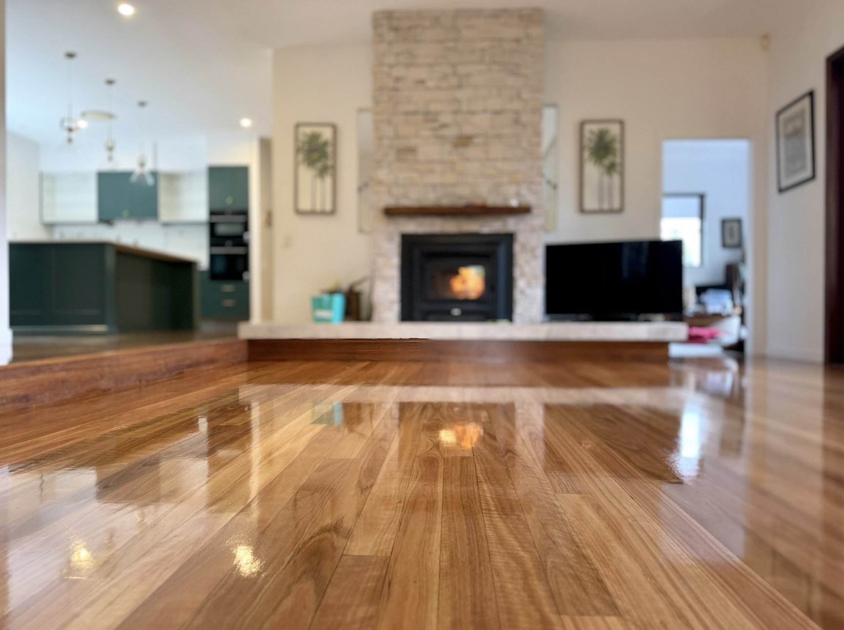 Empty living room with polished wooden floor, stone fireplace, and TV, view from the floor level.