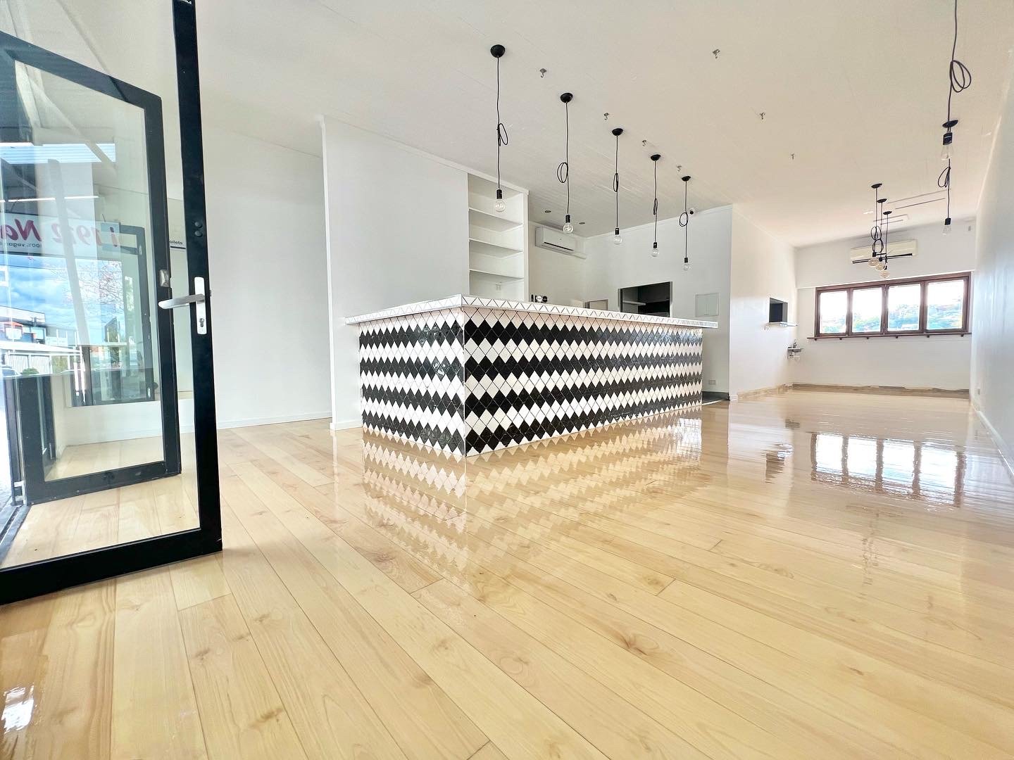 Empty room with a modern counter featuring black and white diamond-patterned tiles, large windows, and wooden floors in Brisbane.