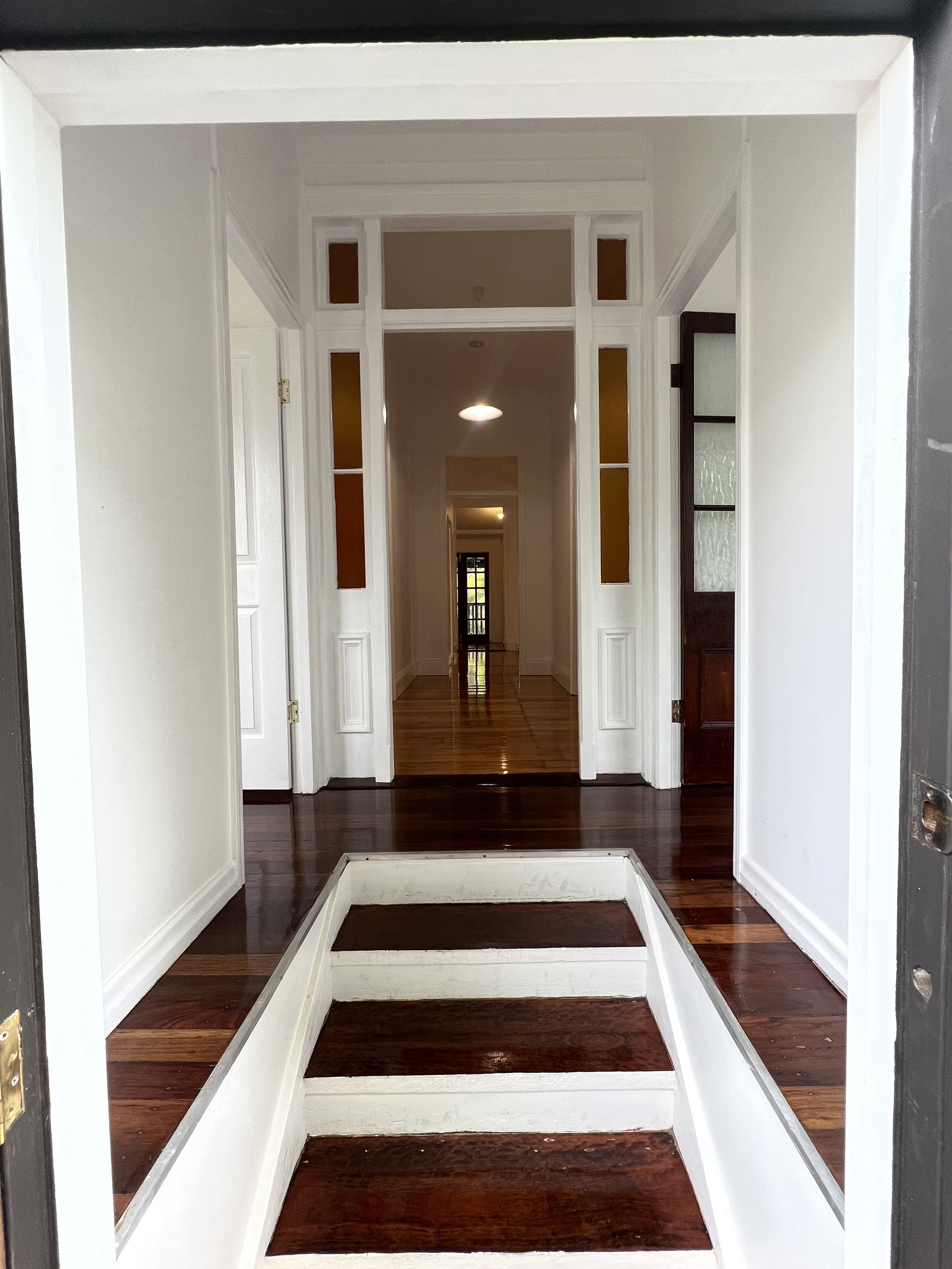 View of a welcoming front entrance with three steps leading into a hallway with white trim, hardwood floors, and multiple doorways leading to rooms in a house.