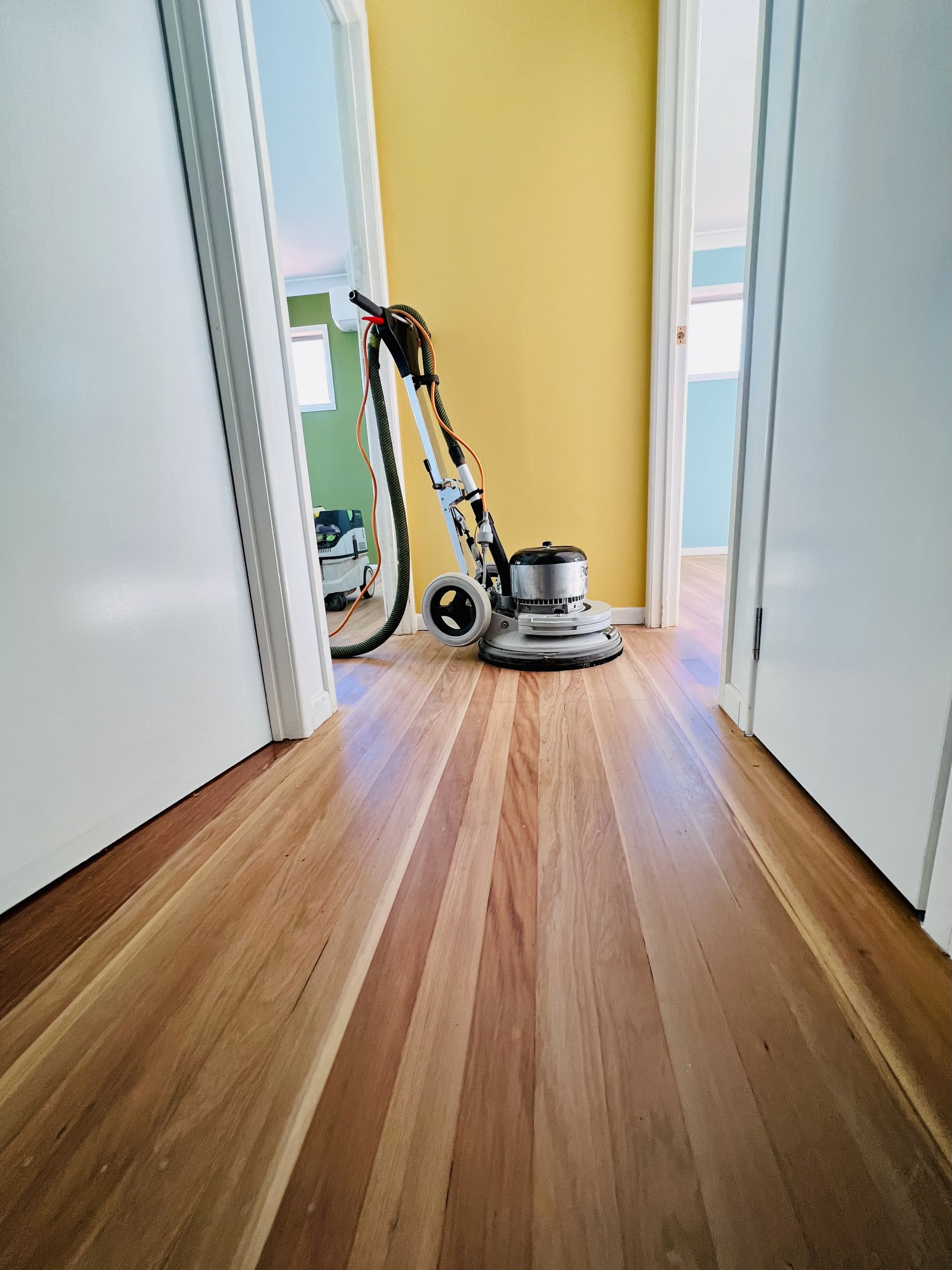 Partially sanded hardwood floor in a hallway with a floor sanding machine.