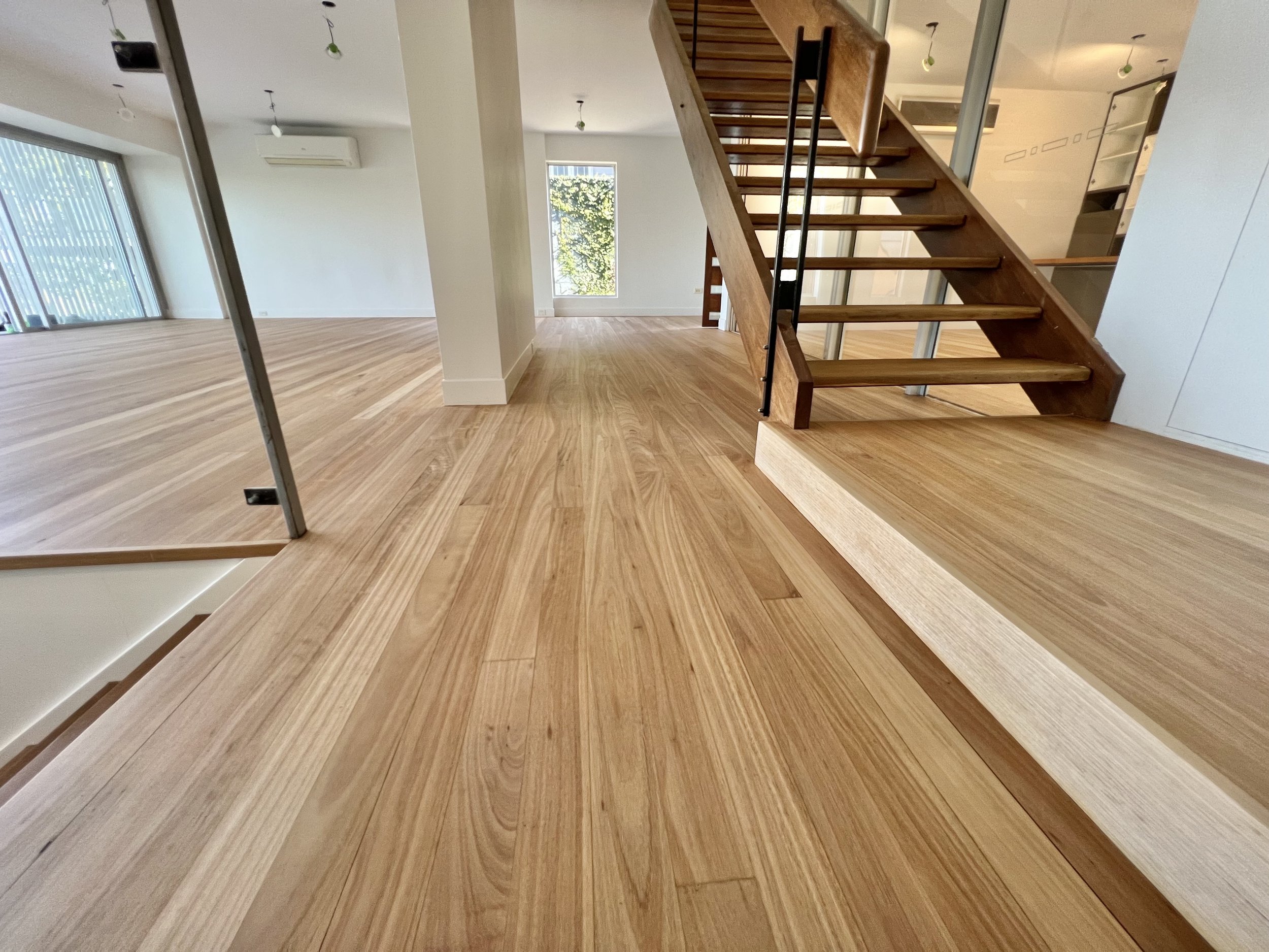 Modern interior with light wood flooring, a staircase, and large windows allowing natural light.