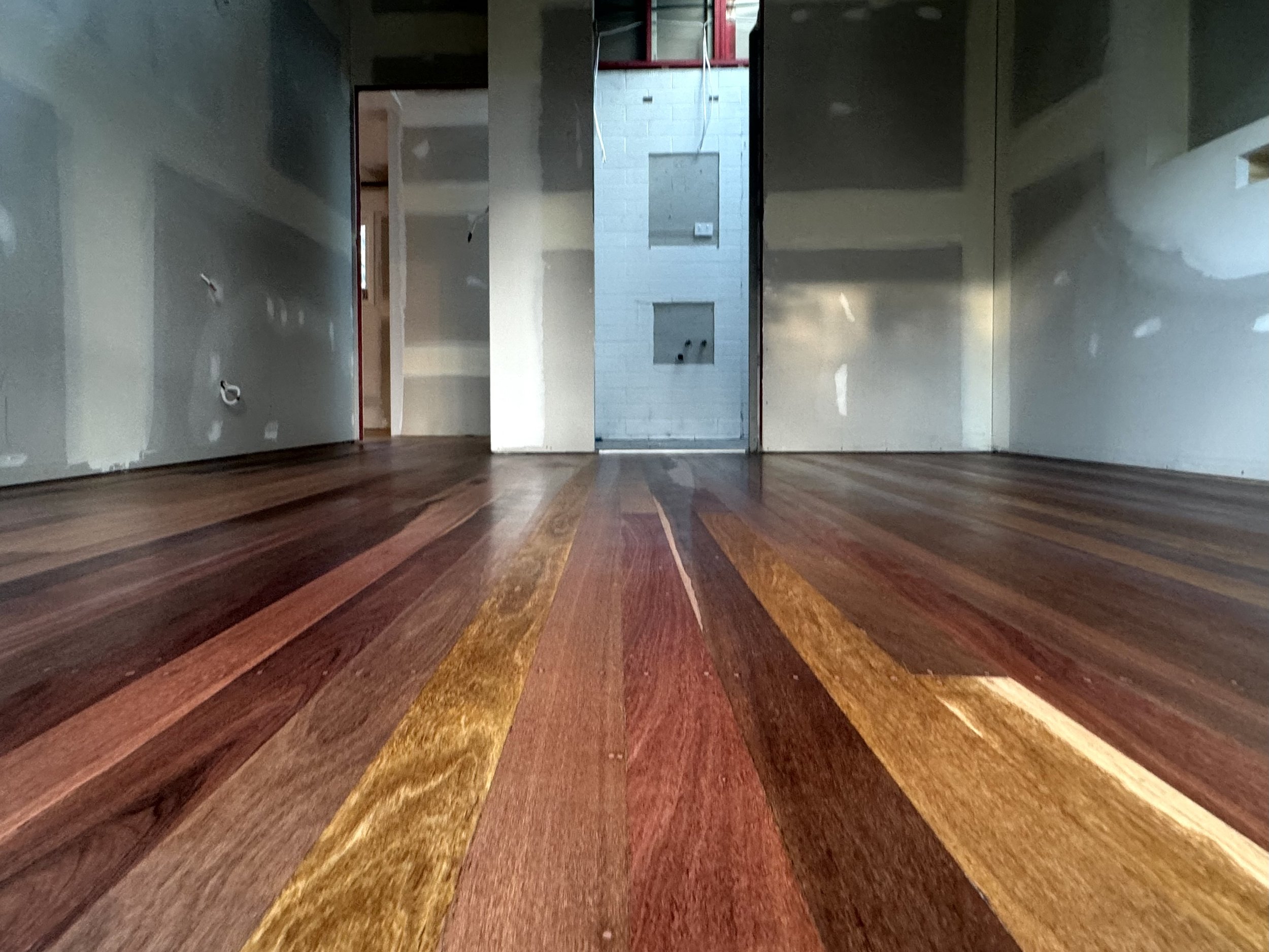 Interior of a room under construction with unfinished drywall and a hardwood floor with multi-colored planks.