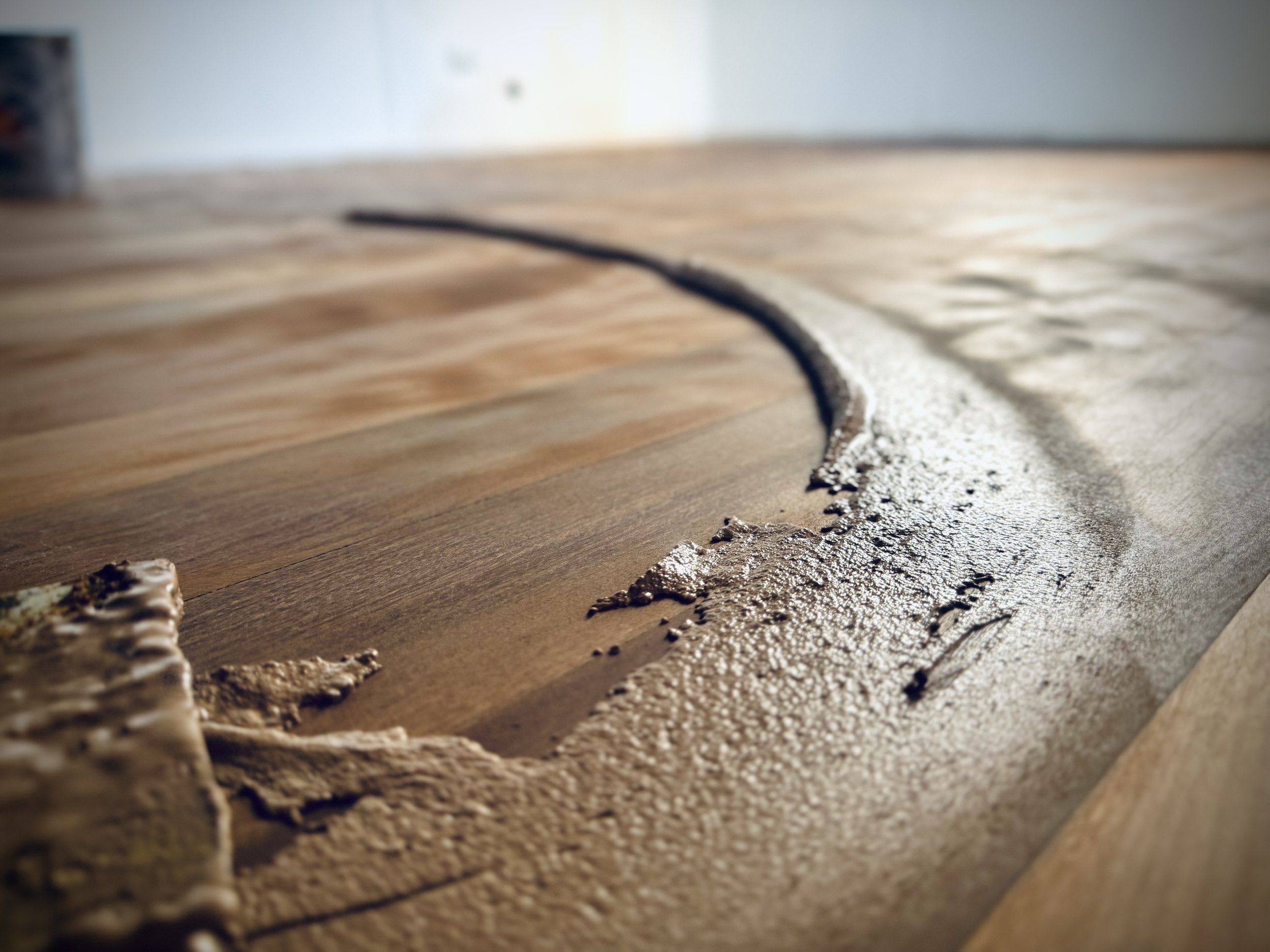 Close-up of a wooden floor with wet glue dripped along the edge during flooring installation.
