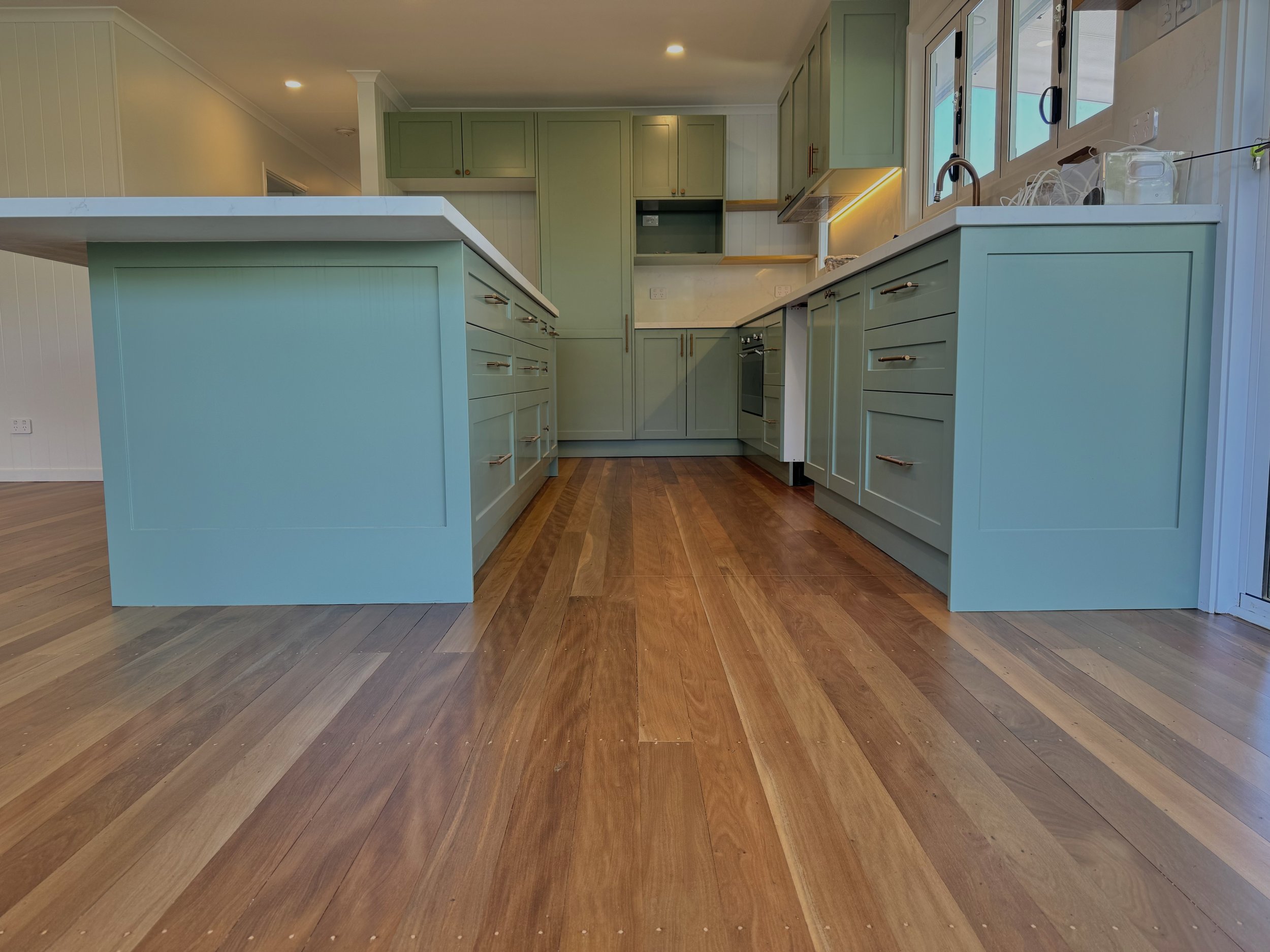 Kitchen with mint green cabinets, white countertops, wooden floors, and a side door.