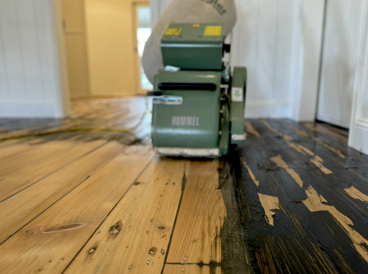 A floor sanding machine in use on a wooden floor, with part of the floor partially stripped and the other part still with finish intact.