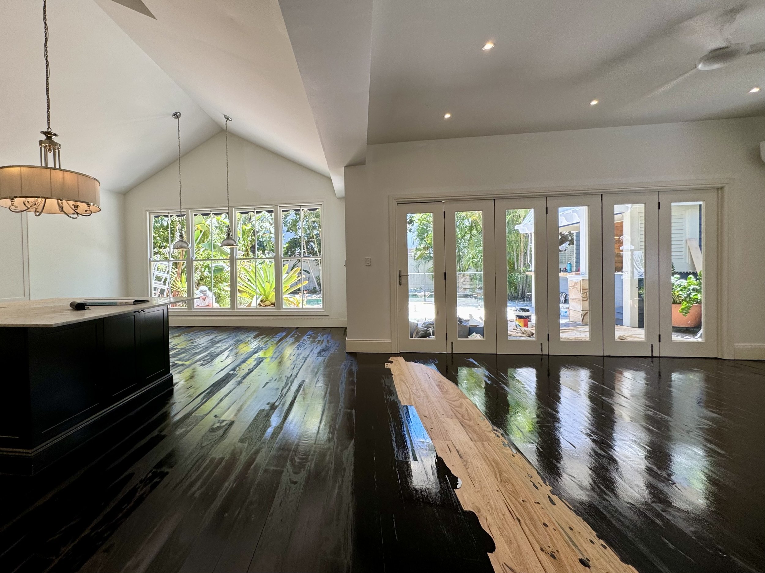 Living room with dark wood flooring and white walls, large window, and double glass doors leading outside, with visible greenery and patio area.