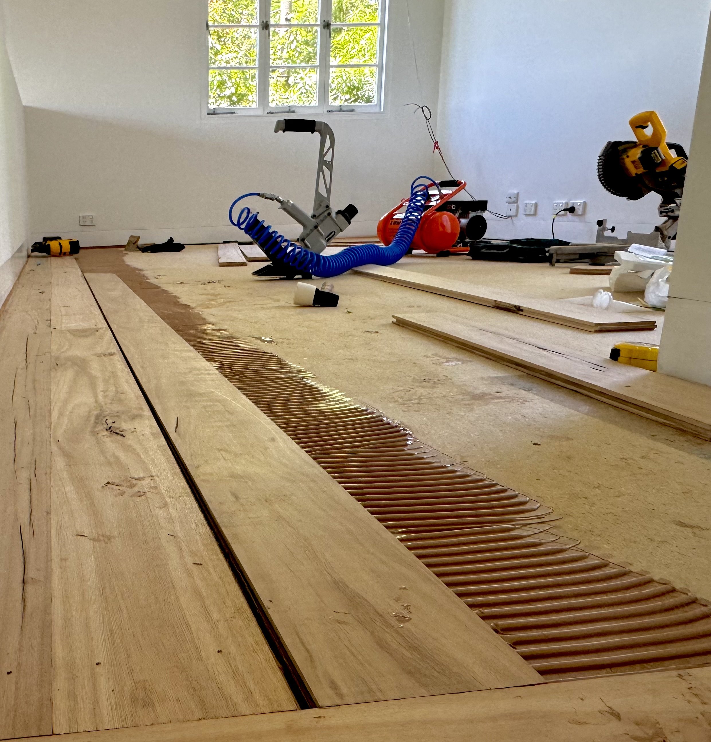Interior of a room under renovation with wooden flooring, tools, and construction equipment.