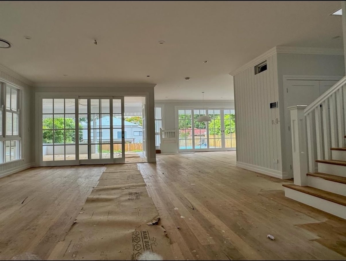 Empty, unfinished living room with large windows, sliding glass doors leading to an outdoor patio, and a staircase with wooden steps and white railing.