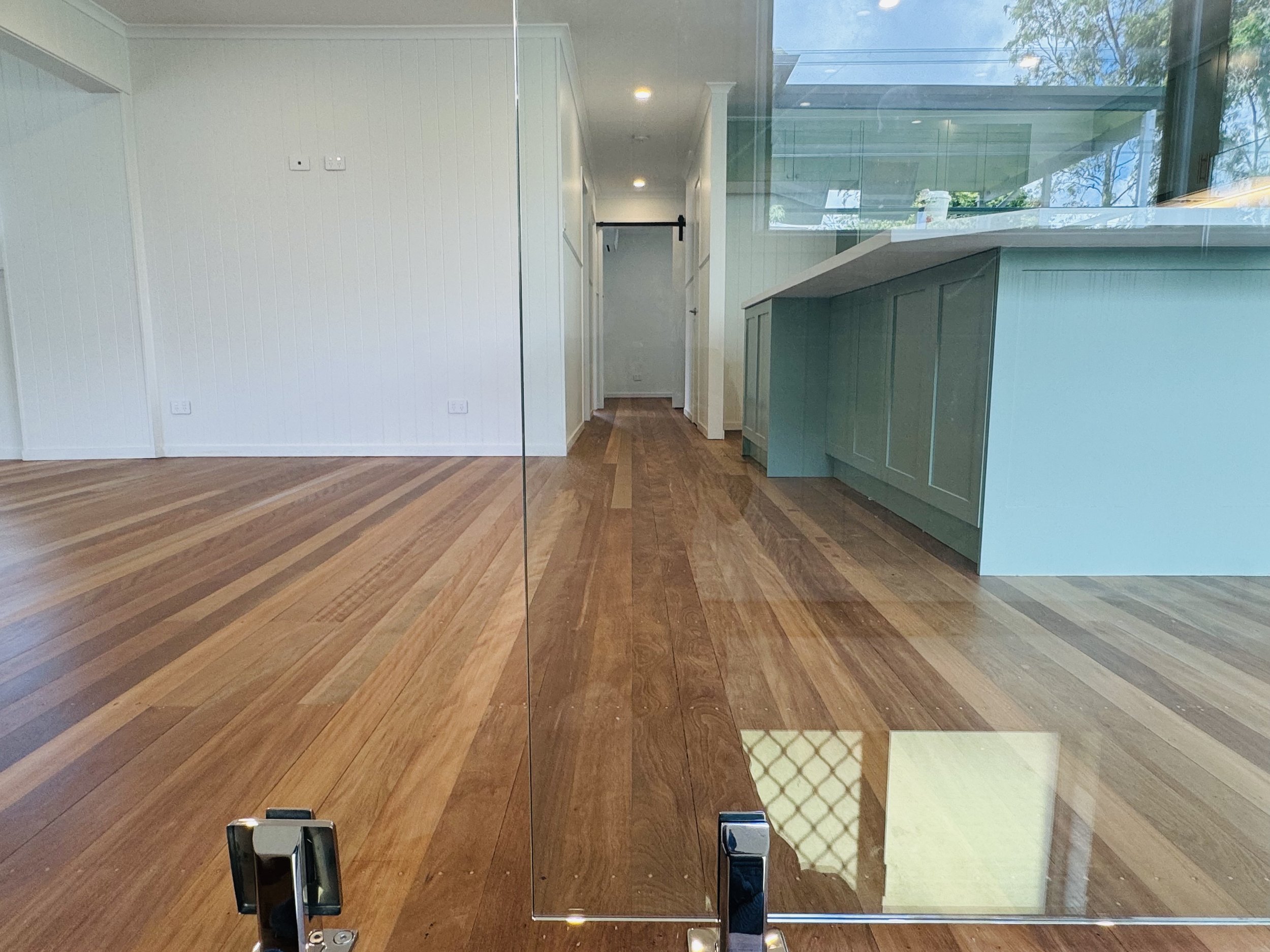 Interior view of a modern room with wooden flooring, glass partition, and a kitchen area with turquoise cabinets.