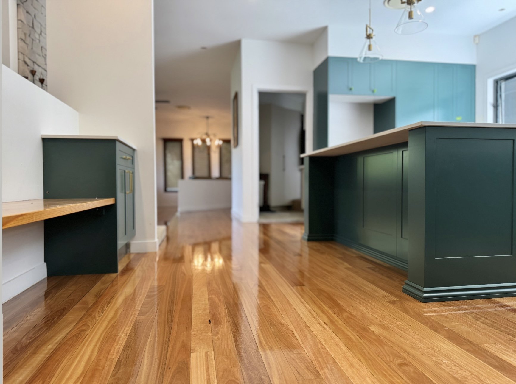 Interior view of a modern home with hardwood floors, teal kitchen cabinets, and a white and blue wall. There are pendant lights hanging from the ceiling.