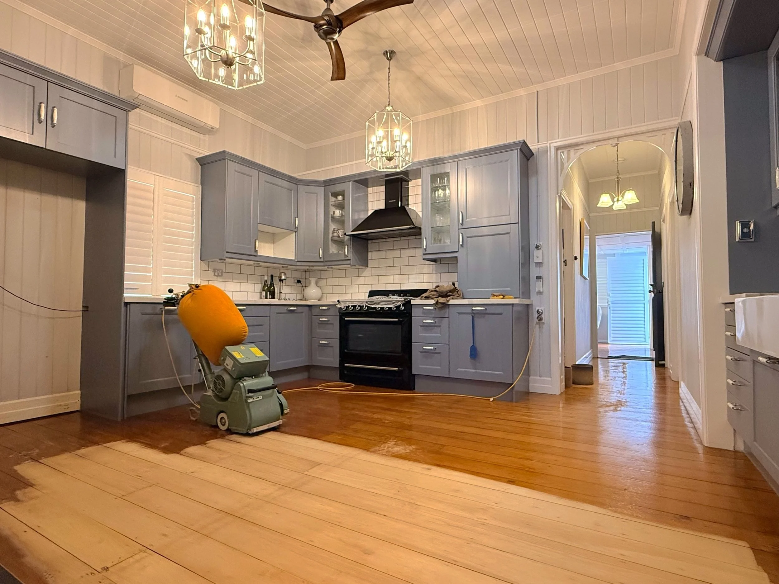 Hoop pine floor half-sanded in a Windsor Queenslander kitchen, drum sander on the job