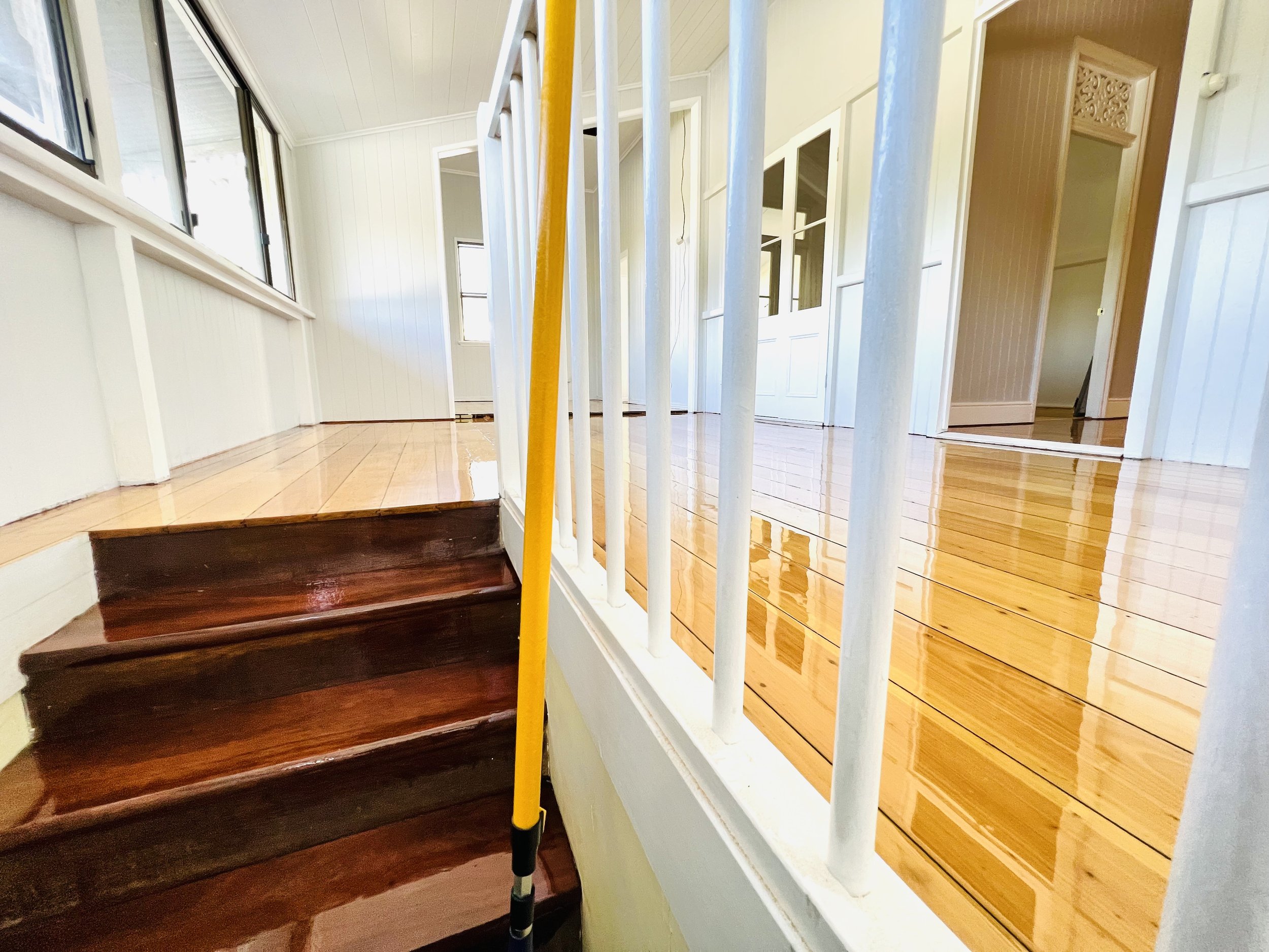 Interior of a house with polished wooden floors, white walls, and stairs with a yellow broom leaning against the railing.
