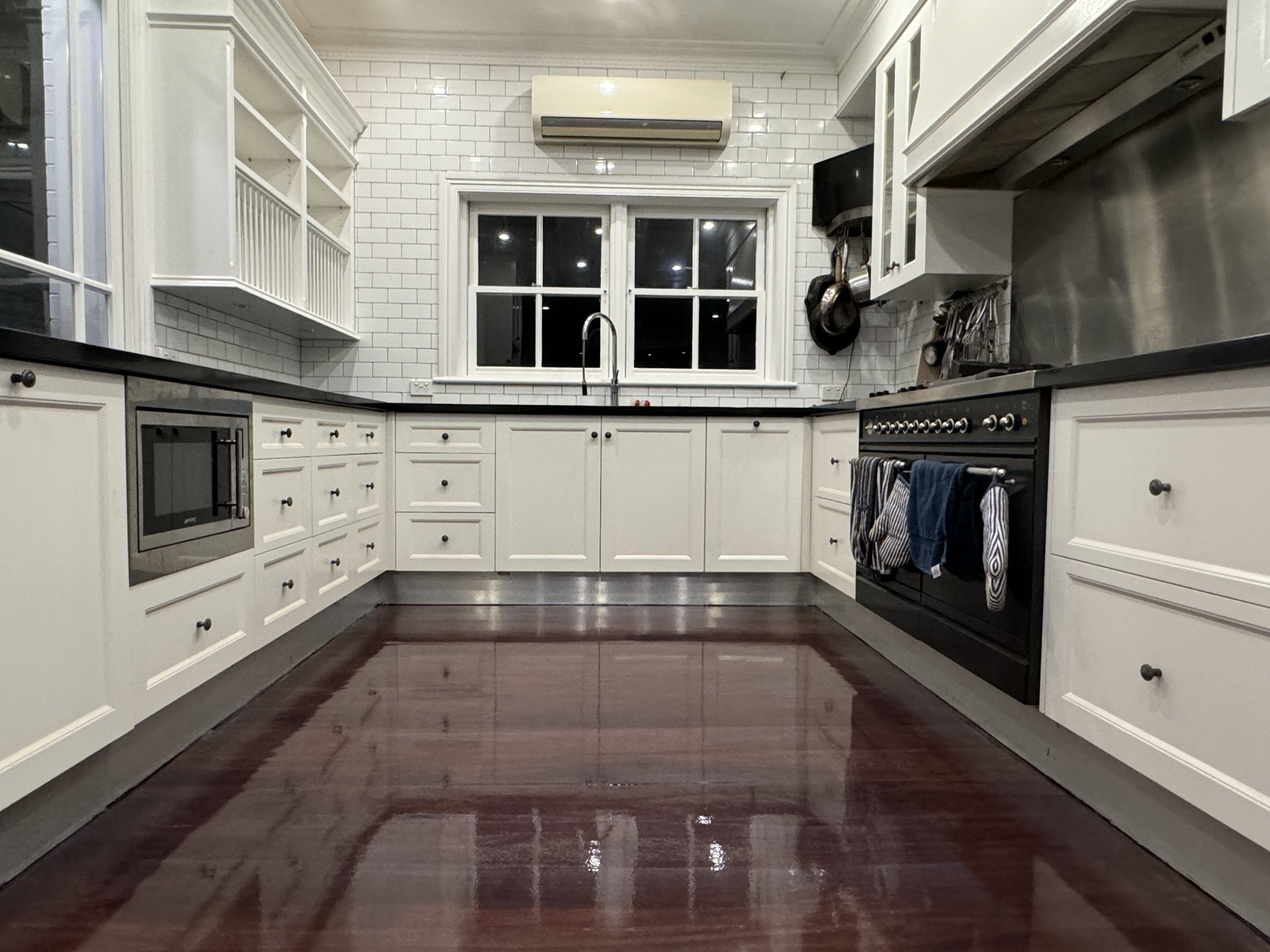 Modern kitchen with white cabinetry, black countertops, a black stove with towels hanging, a window above the sink, and hardwood floors.