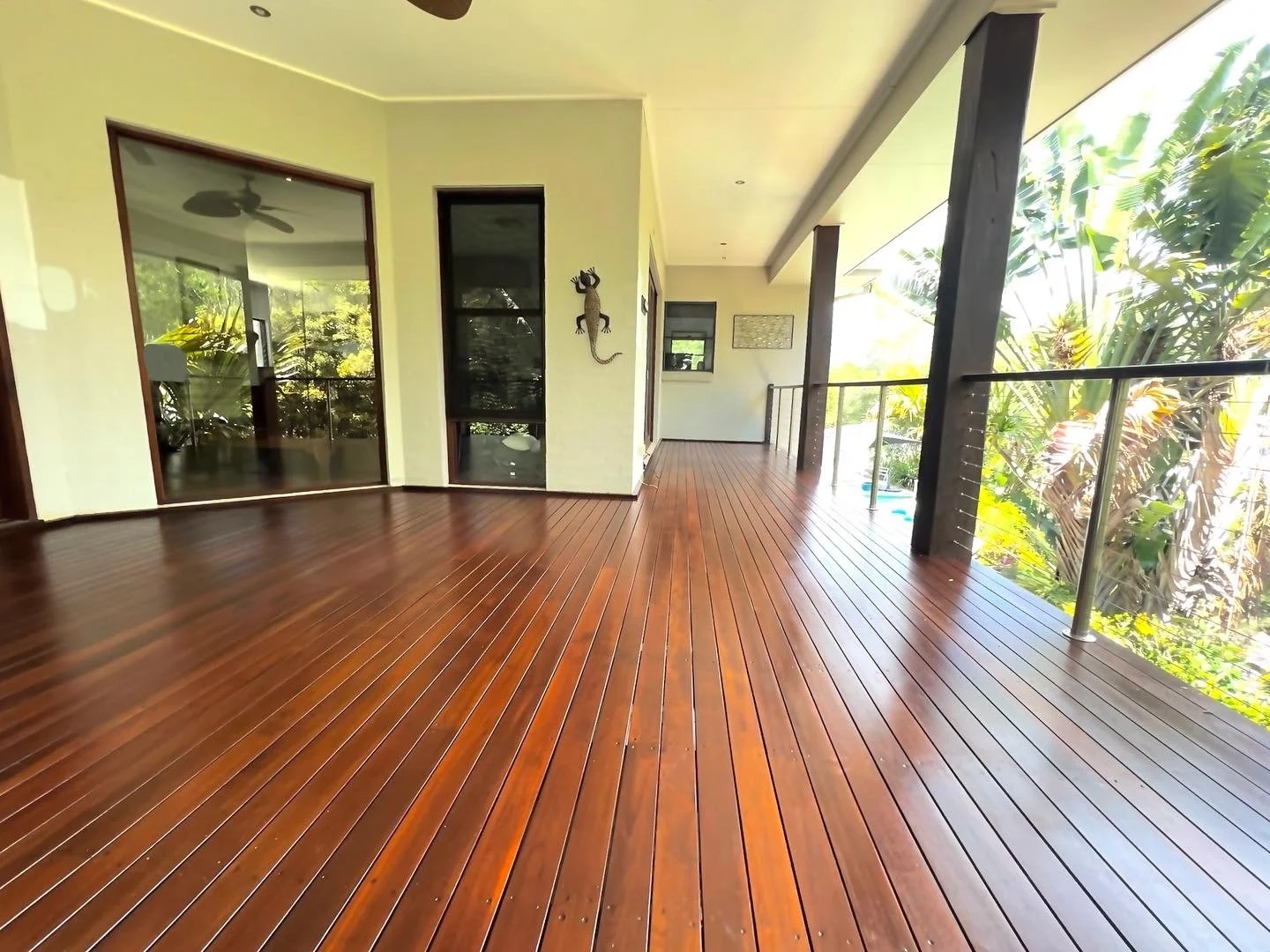 Wide view of a wrap-around deck with a glass balustrade, timber freshly finished