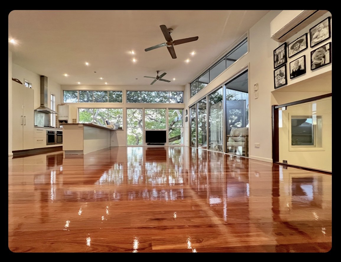 Spacious open-plan living area with hardwood floors, large windows, modern kitchen, and ceiling fans.