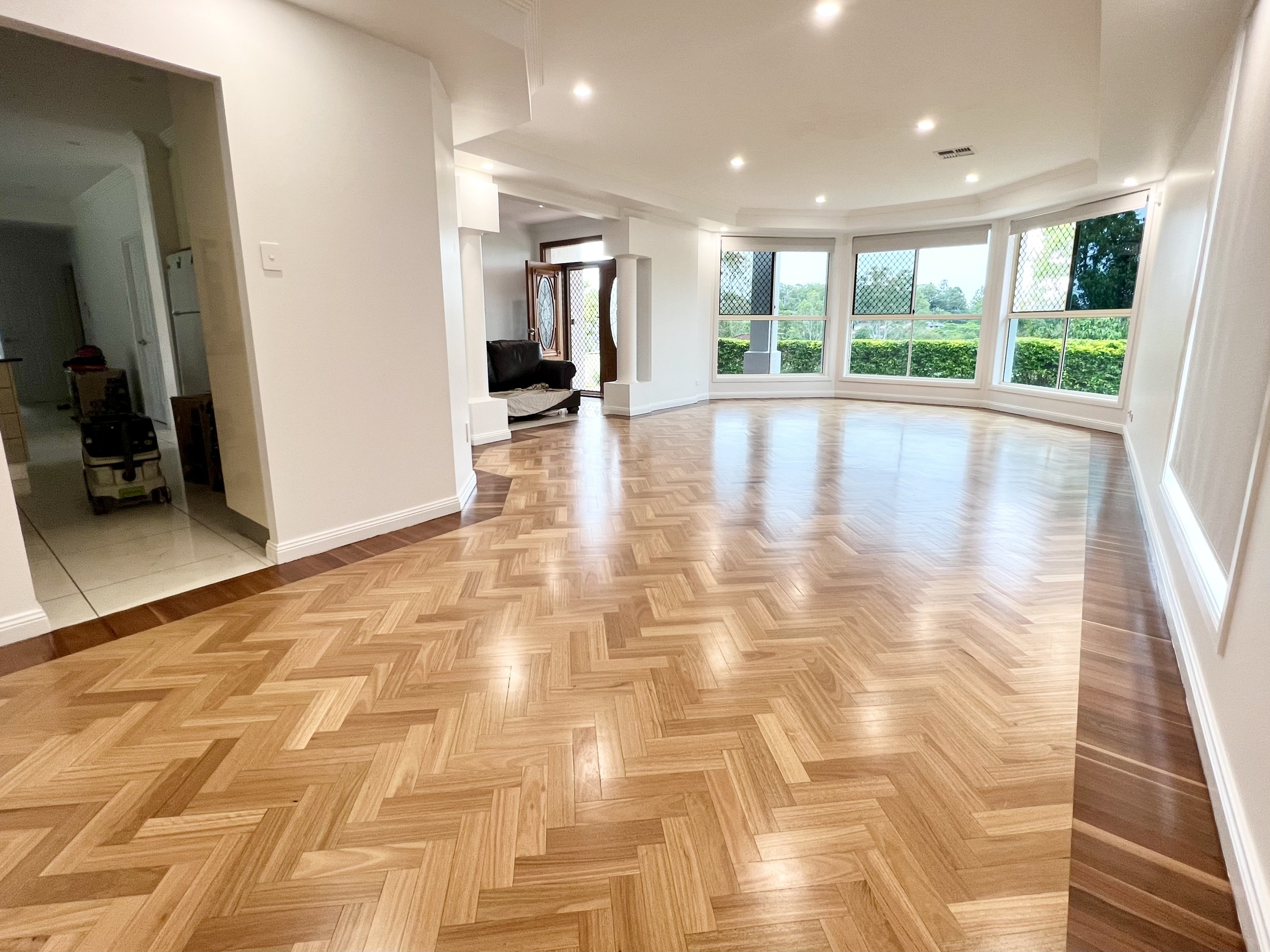 Empty living room with large windows, hardwood floor, and white walls.