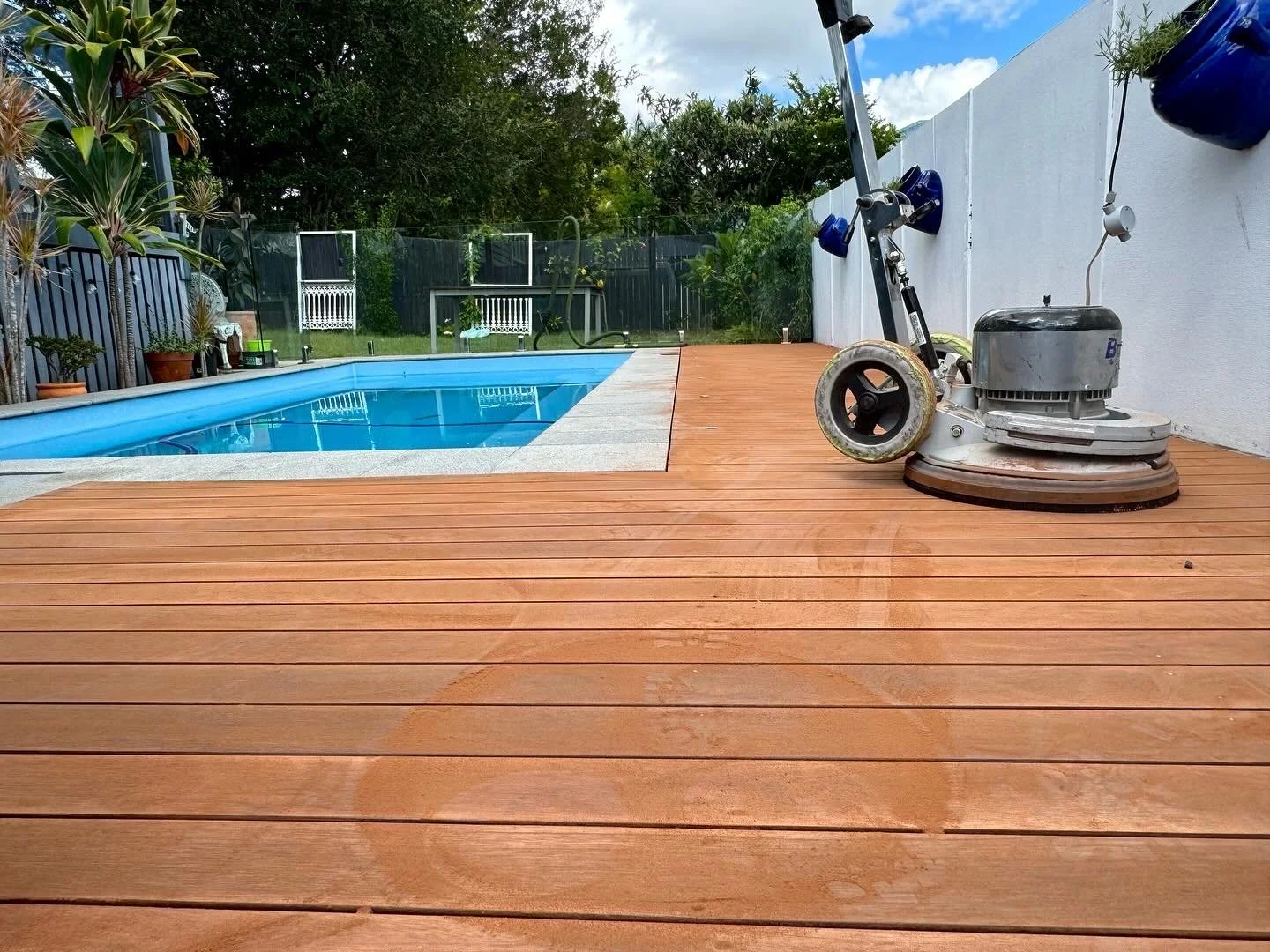 The same Brisbane pool deck mid-job, sanded back to bare timber with the floor machine still on the boards