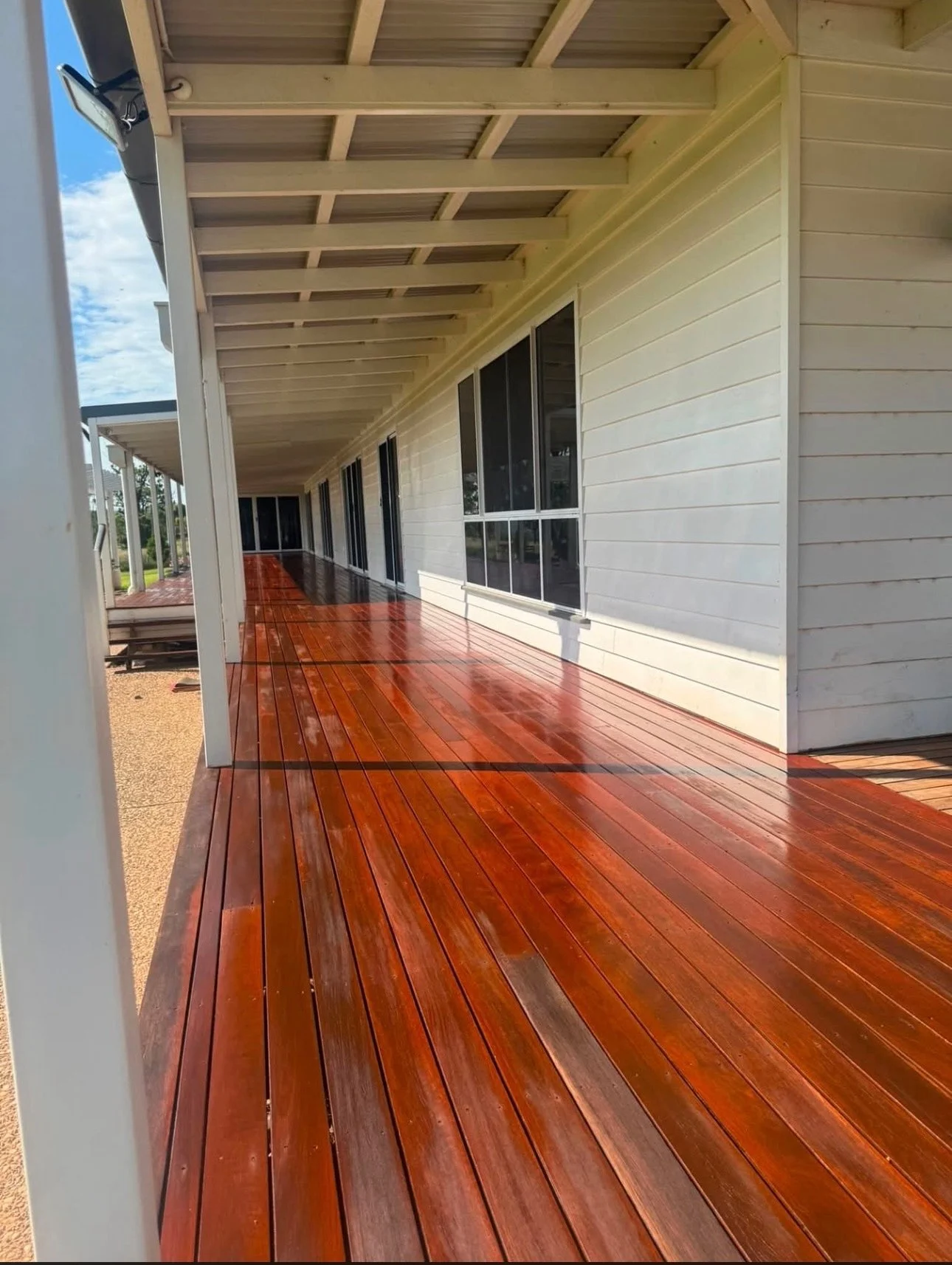 Long covered verandah deck alongside a white weatherboard home after sanding and re-coating