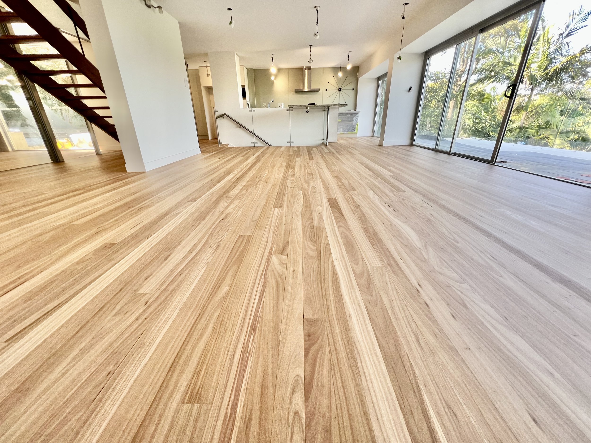 Spacious living area with light wood flooring, large sliding glass doors, and a view of trees outside.