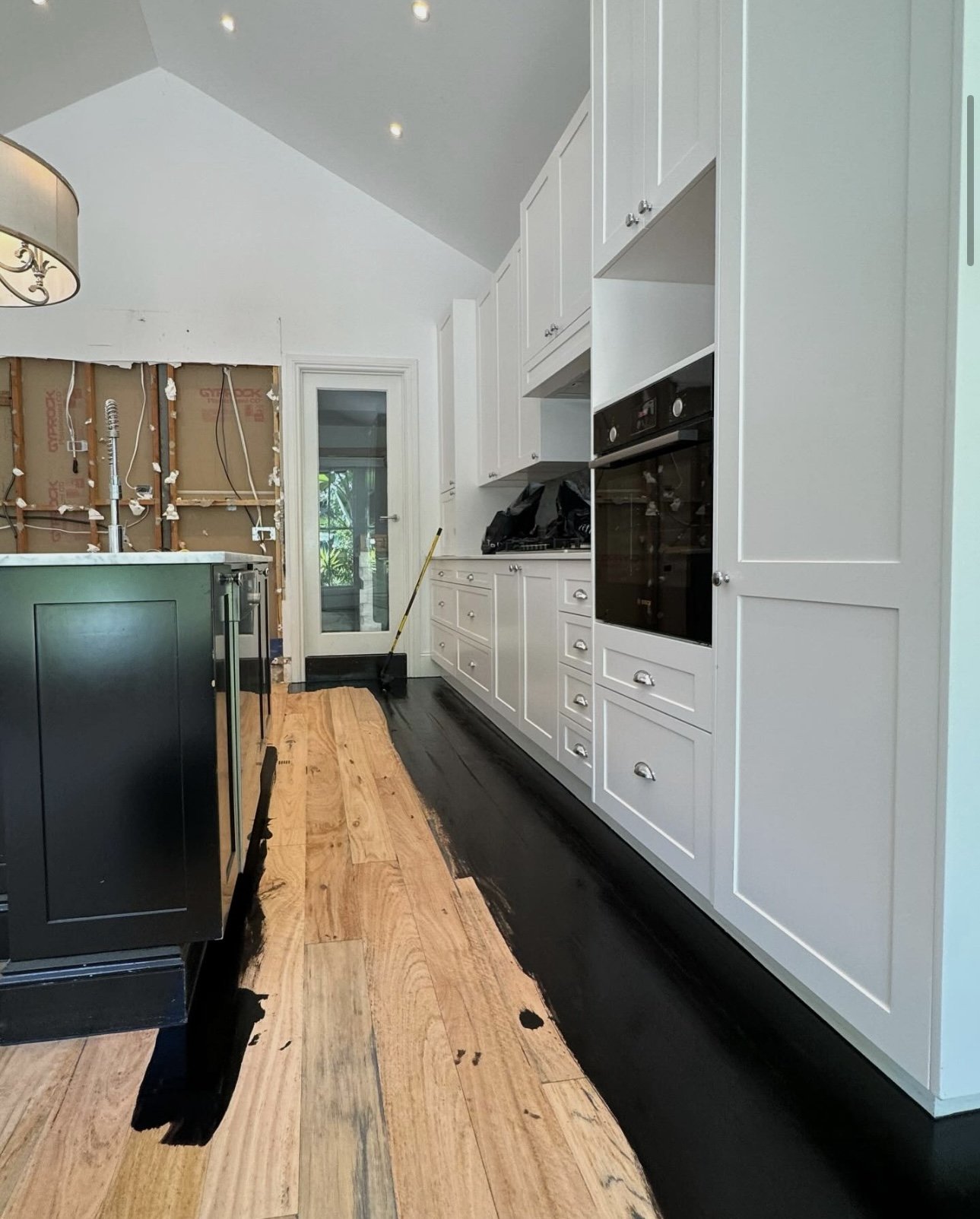 Kitchen with white cabinets, black appliances, a partially finished wooden floor, and a construction area at the back with exposed wall and wiring.