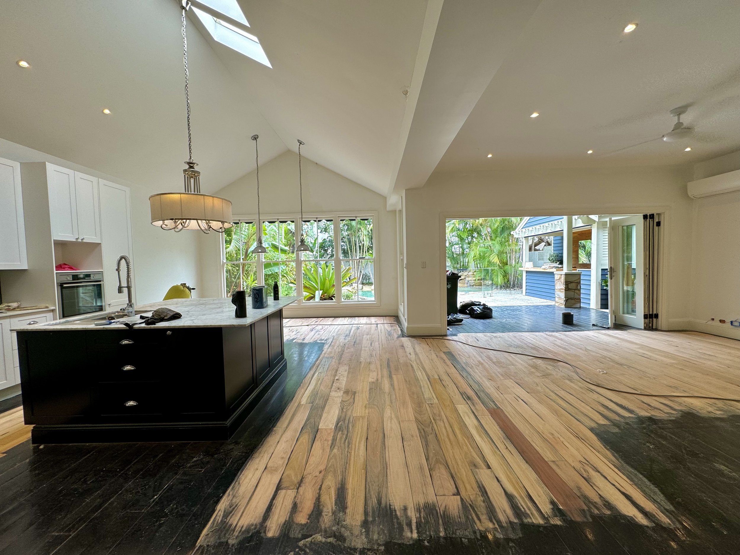 Open plan kitchen and living room with hardwood floors and large windows, with ongoing floor refinishing work.