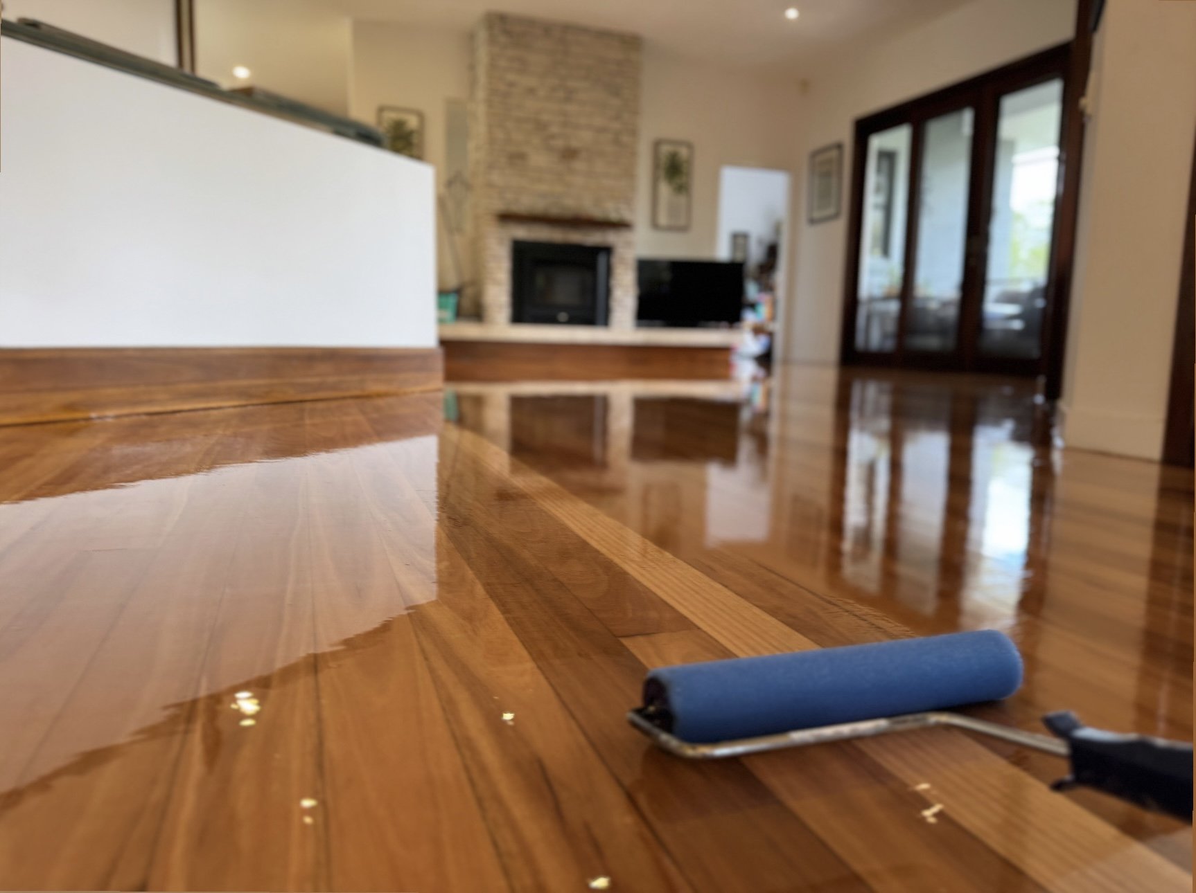 Close-up of a wood table with a roller paintbrush resting on it, with a blurred living room in the background.