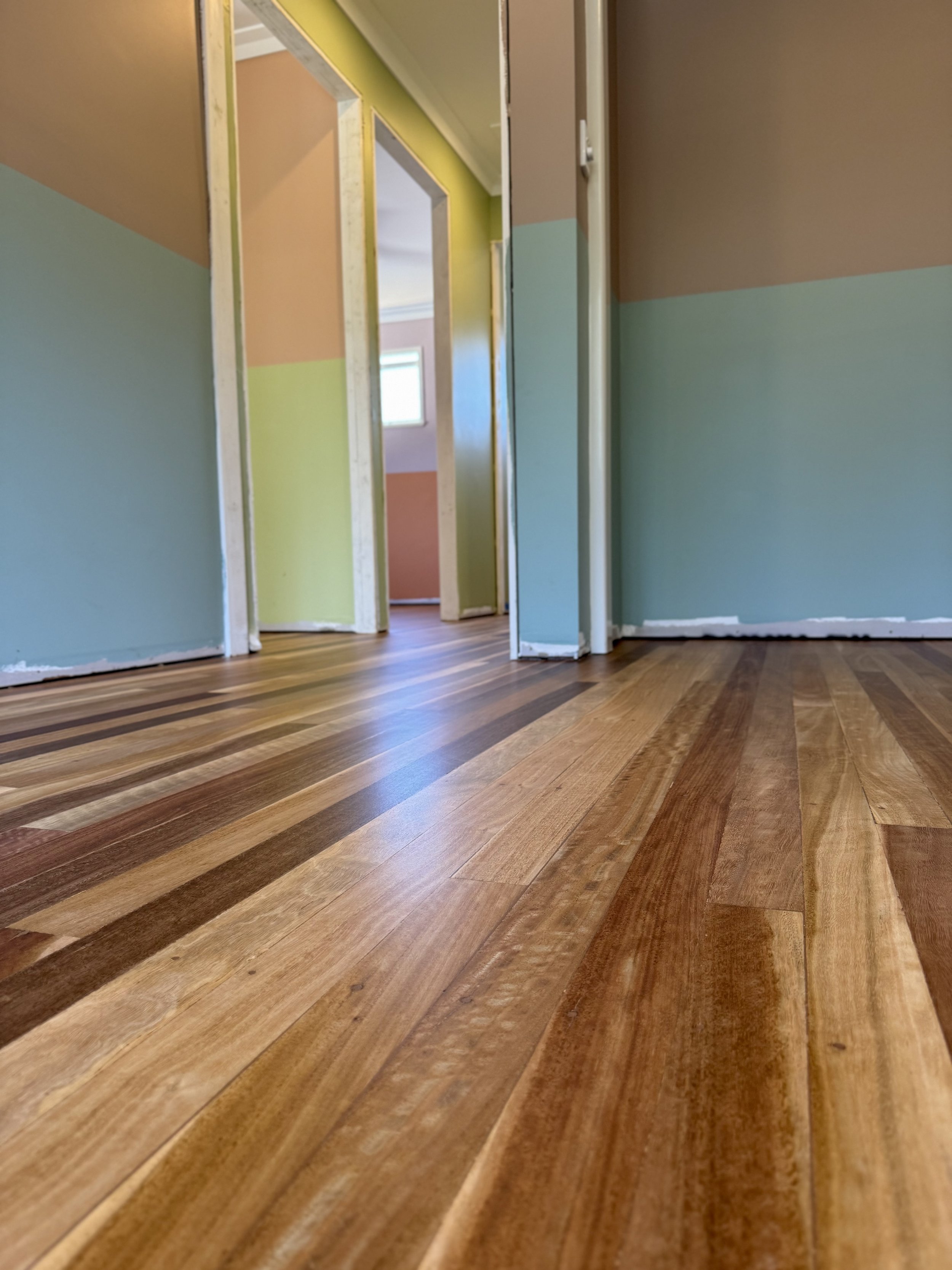 Interior view of a house with unfinished door frames and painted walls, showing hardwood flooring.