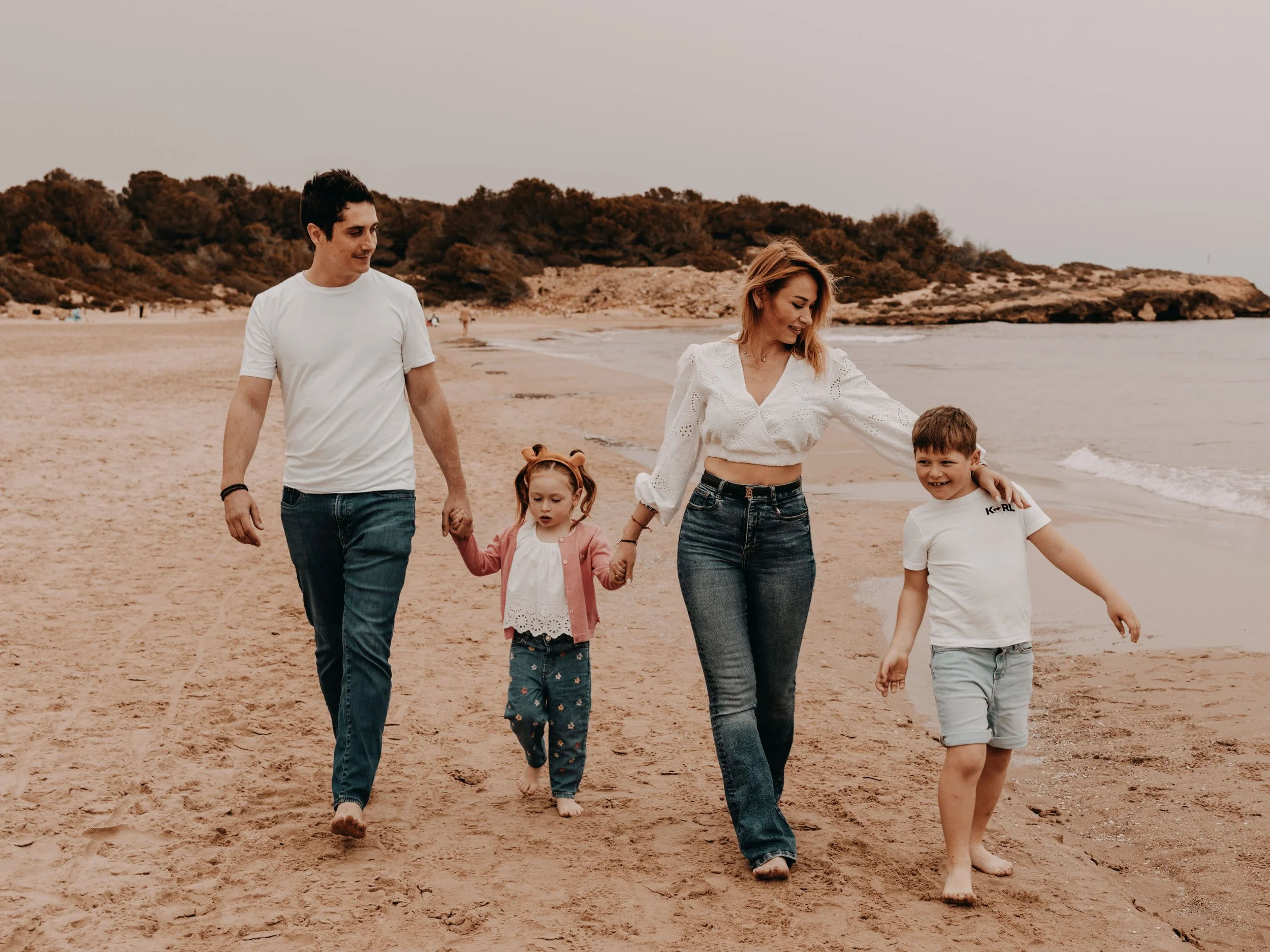 Familia caminando por la playa, tomando de las manos a los niños y disfrutando del día.