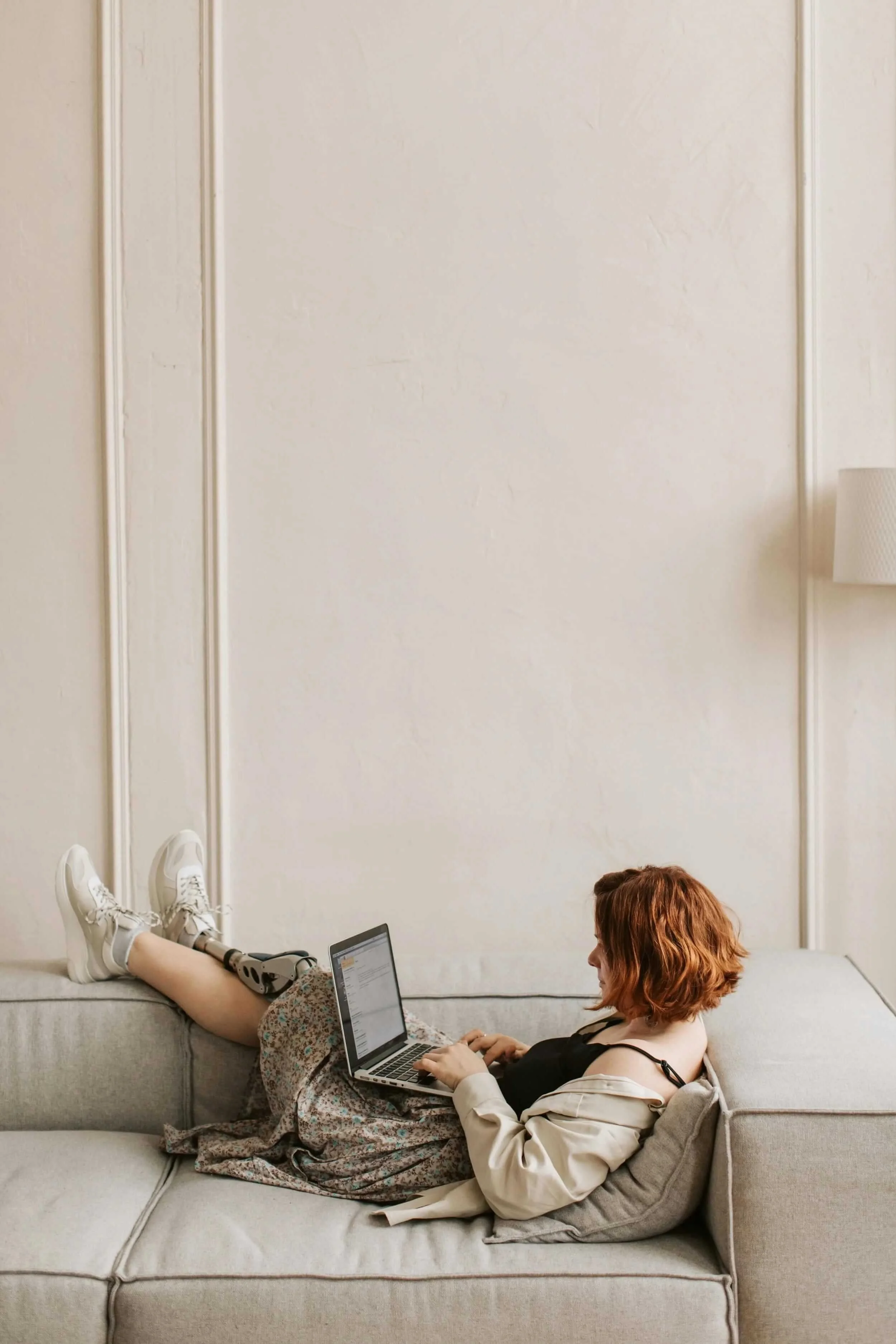 red haired woman sitting on coach with feet up and working on her laptop