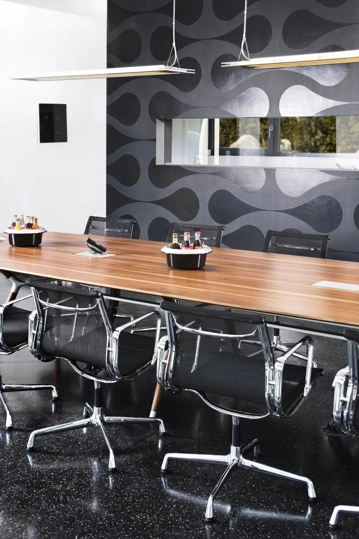 Moderner Besprechungsraum der NOBRA GmbH mit großem Holztisch, ergonomischen Stühlen, Getränkesets und dunkler Designwand für professionelle Meetings.