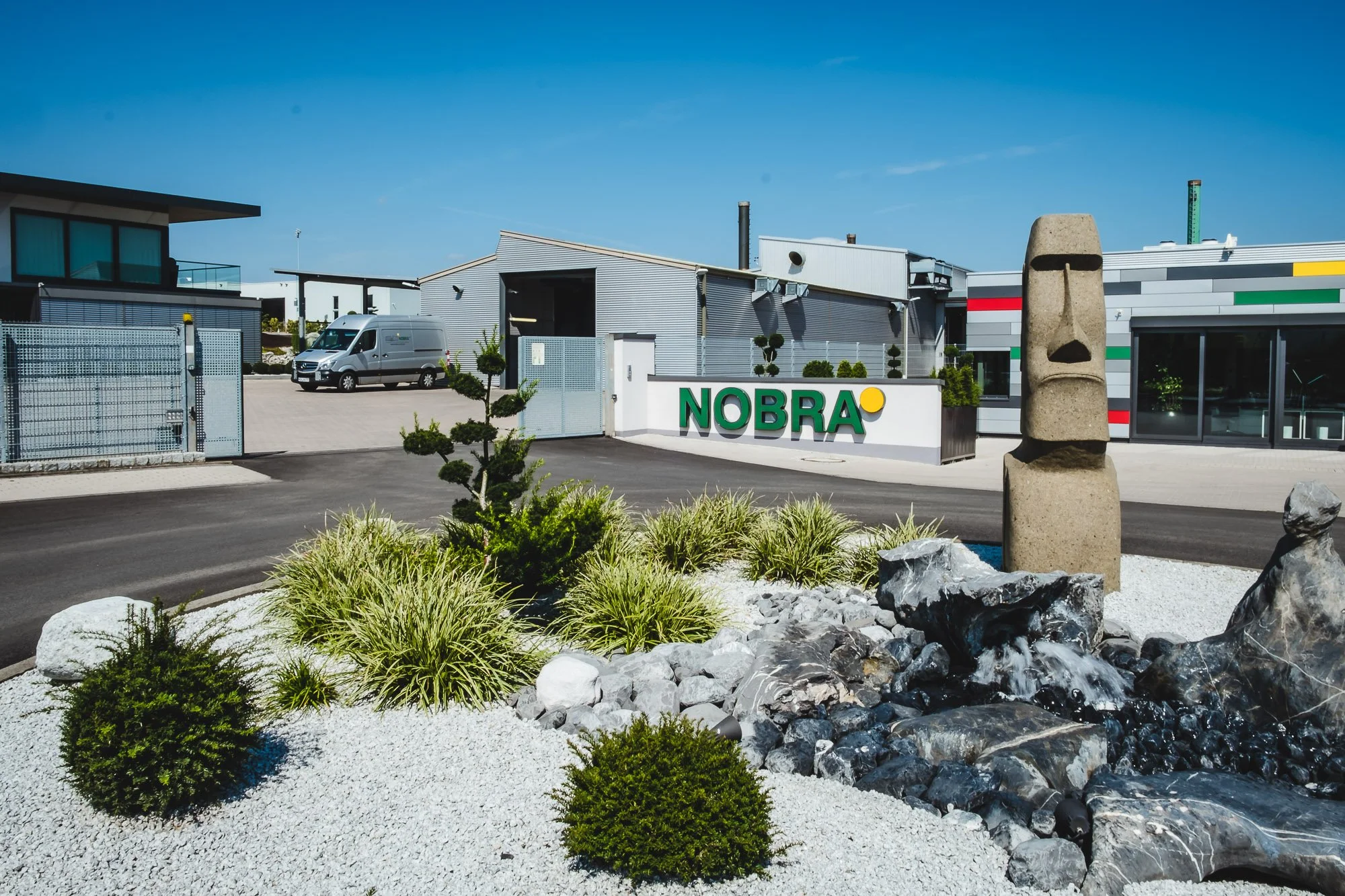 NOBRA GmbH Standort mit Firmenlogo, modernem Gelände und gestalteter Außenanlage als Zentrum für Recycling und Rohstoffrückgewinnung.“