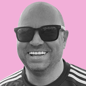 A smiling man wearing sunglasses against a pink background.
