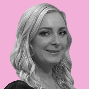 Black and white portrait of a blonde woman smiling, set against a pink background.