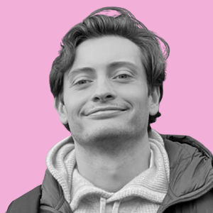 Black and white photo of a young man with wavy hair, smiling, against a pink background.