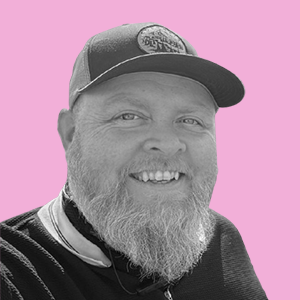 A smiling man wearing a baseball cap against a pink background.