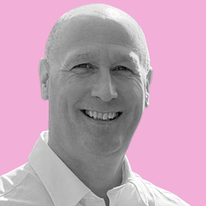 Black and white portrait of a smiling man with short hair against a pink background.