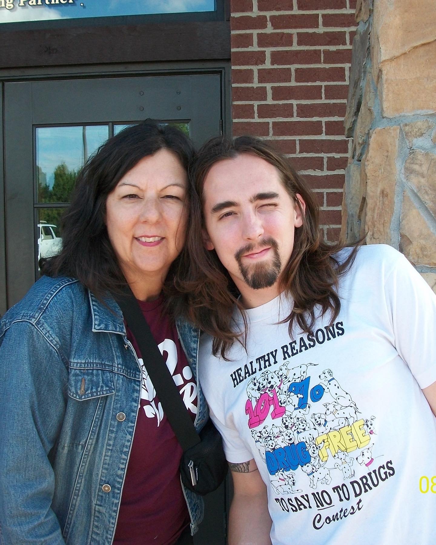 A woman and a man standing close together outside a building, both smiling slightly, with brick and stone walls behind them.