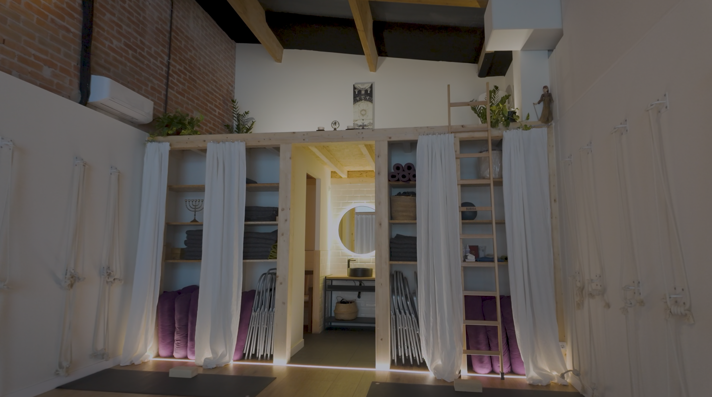 Sala de yoga con colchonetas, bloques y cuerdas en la pared, con luz natural entrando por las ventanas.