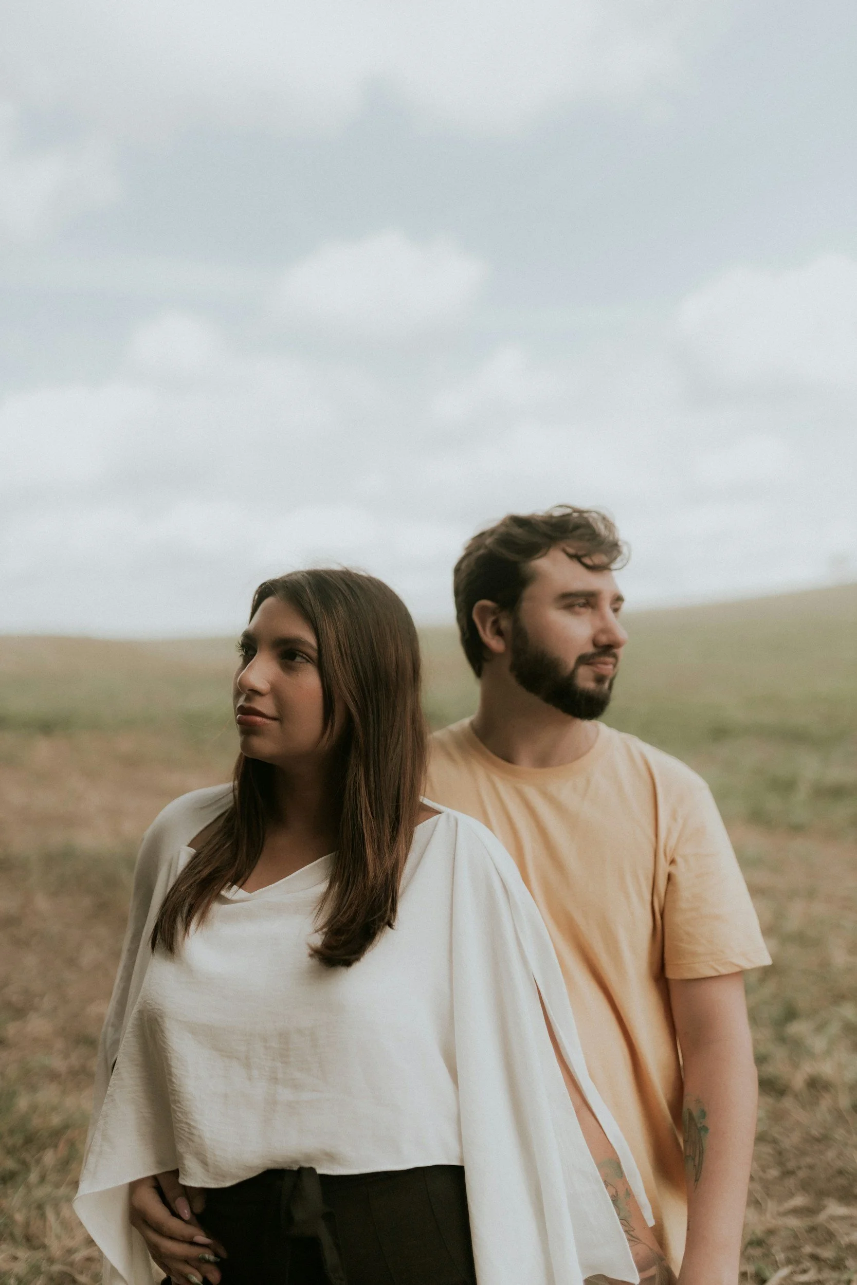 a couple standing in a field, together but looking in opposite directions, symbolizing both connection and autonomy in a relationship
