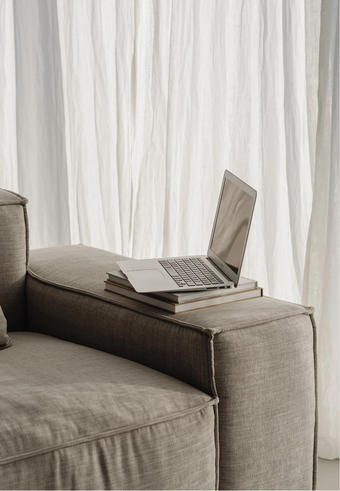A grey sofa with a stack of books and a  laptop on the armrest, representing online couples sessions.