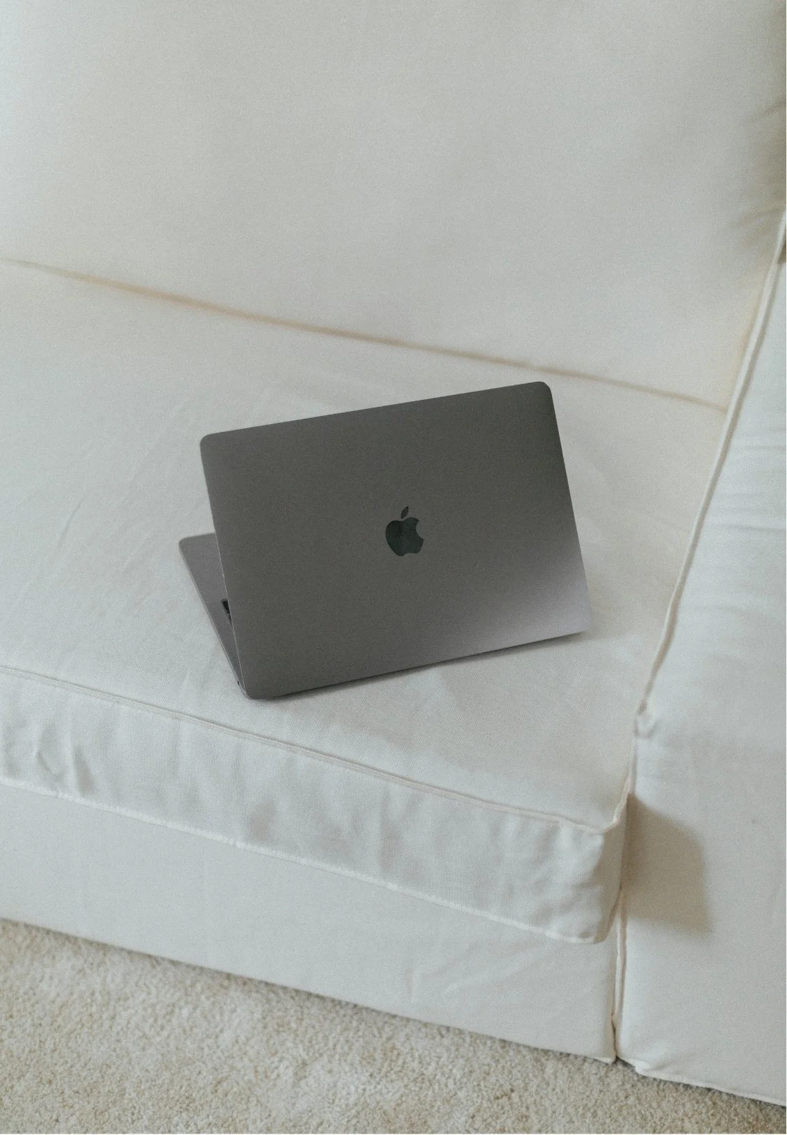 Apple MacBook laptop on a white sofa, representing online therapy sessions